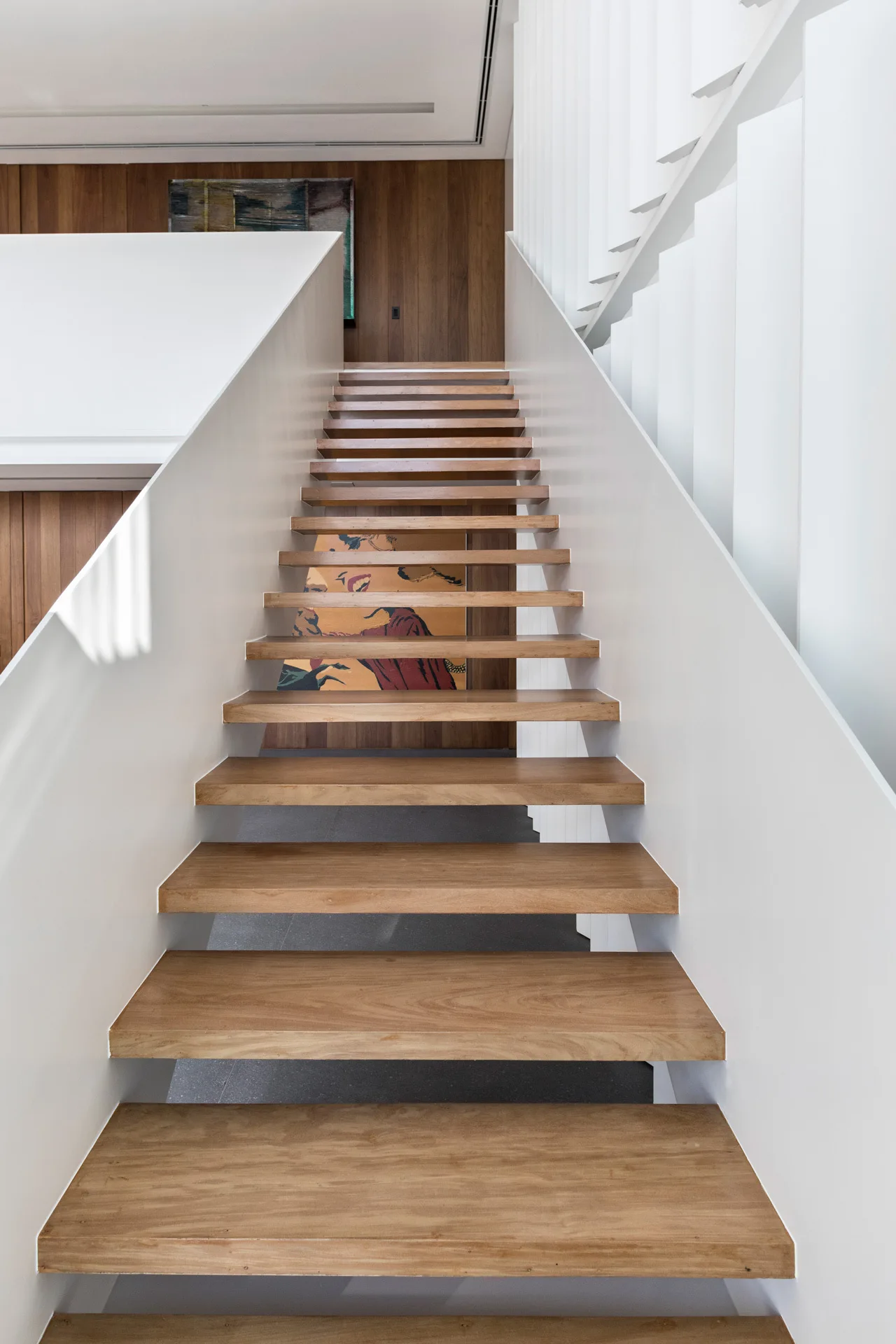 A straight staircase featuring floating wood treads set between solid white side panels against a vertical wood-paneled wall.