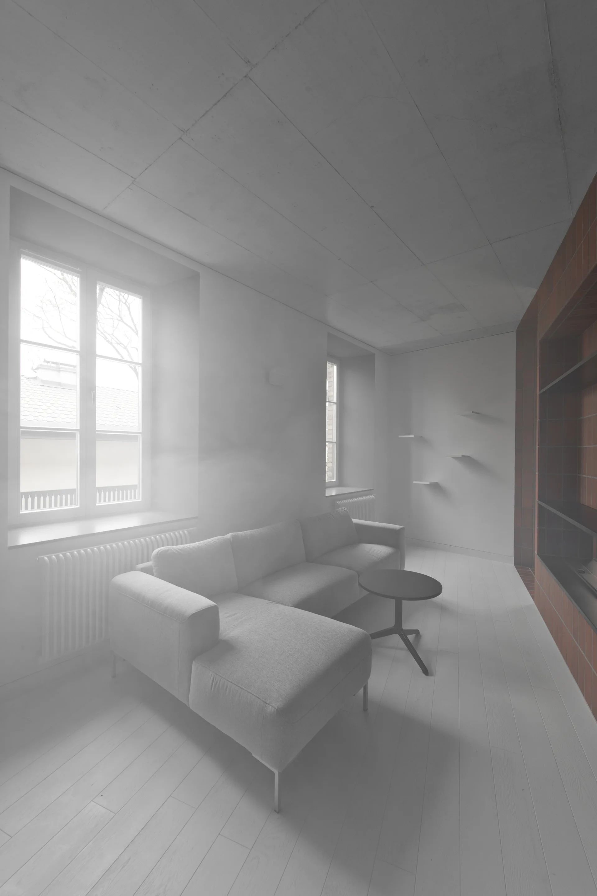 A minimalist living room features a light gray sectional sofa, a concrete panel ceiling, white plank floors, and a terracotta-colored built-in shelving unit.