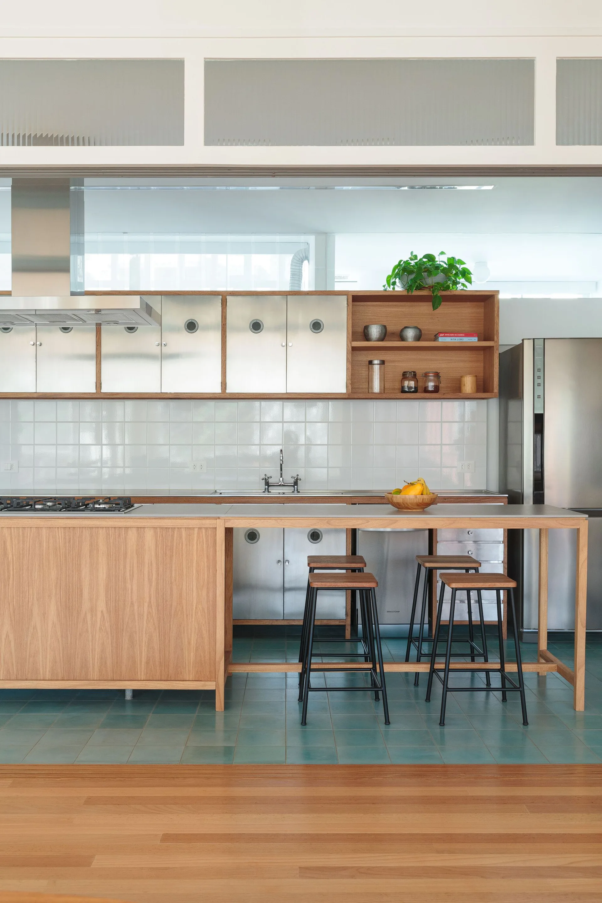 A modern kitchen with a wood kitchen island, stainless steel upper cabinets, a white tiled backsplash, and large teal floor tiles.