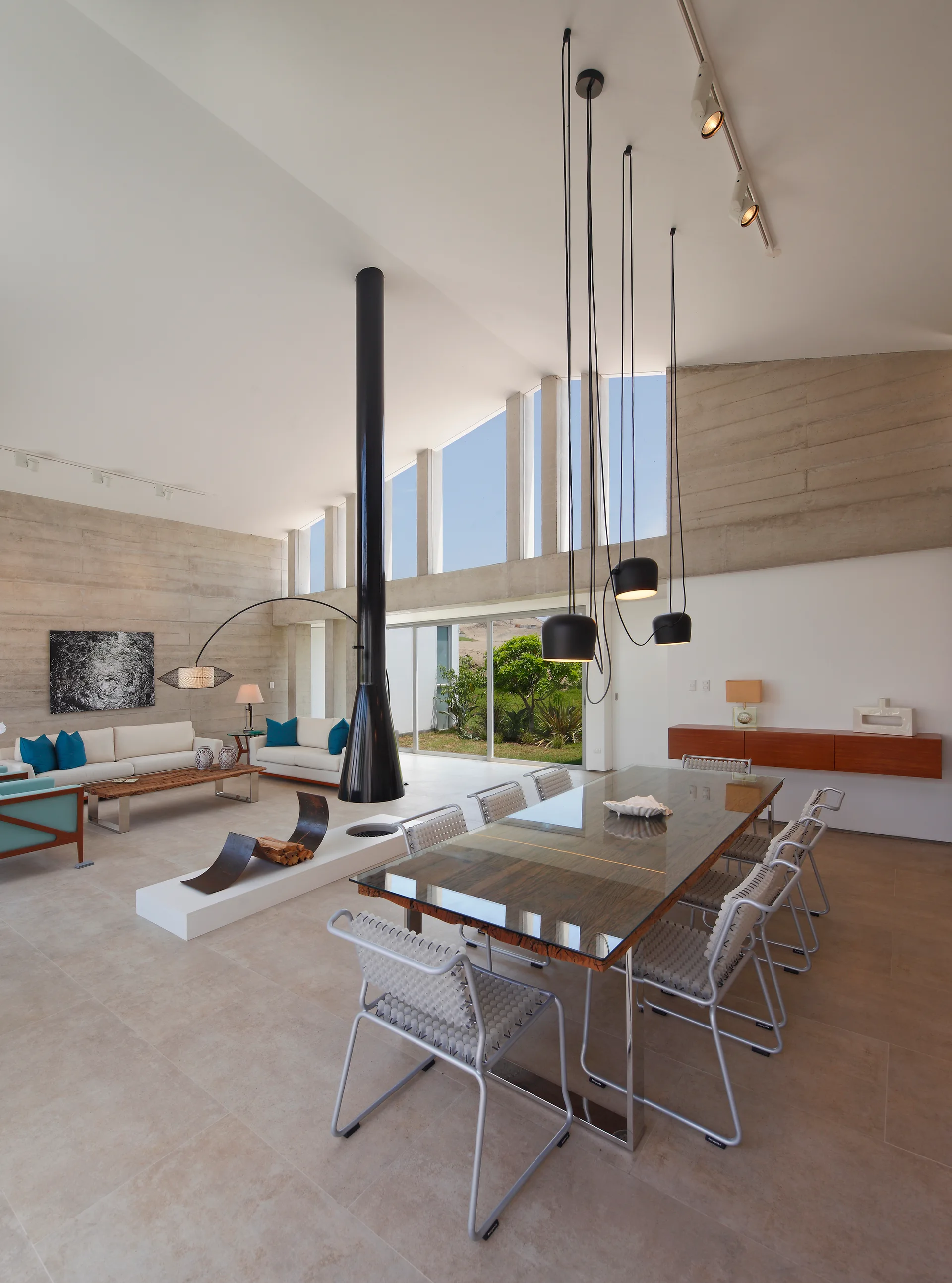 A modern open-plan living and dining room with a suspended black fireplace, textured concrete walls, and a large dining table.