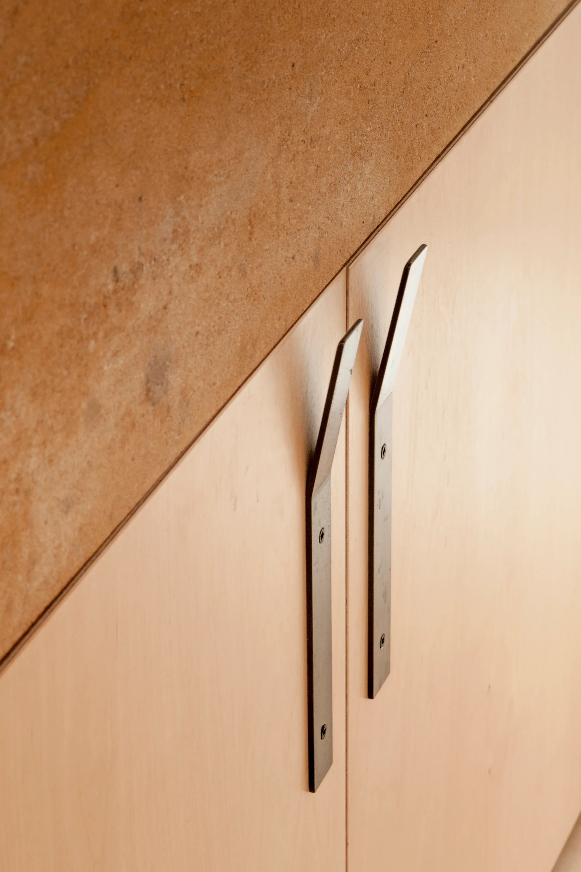 Flat-panel light wood veneer cabinet doors feature angular black metal pull handles beneath a textured brown stone-like countertop surface.