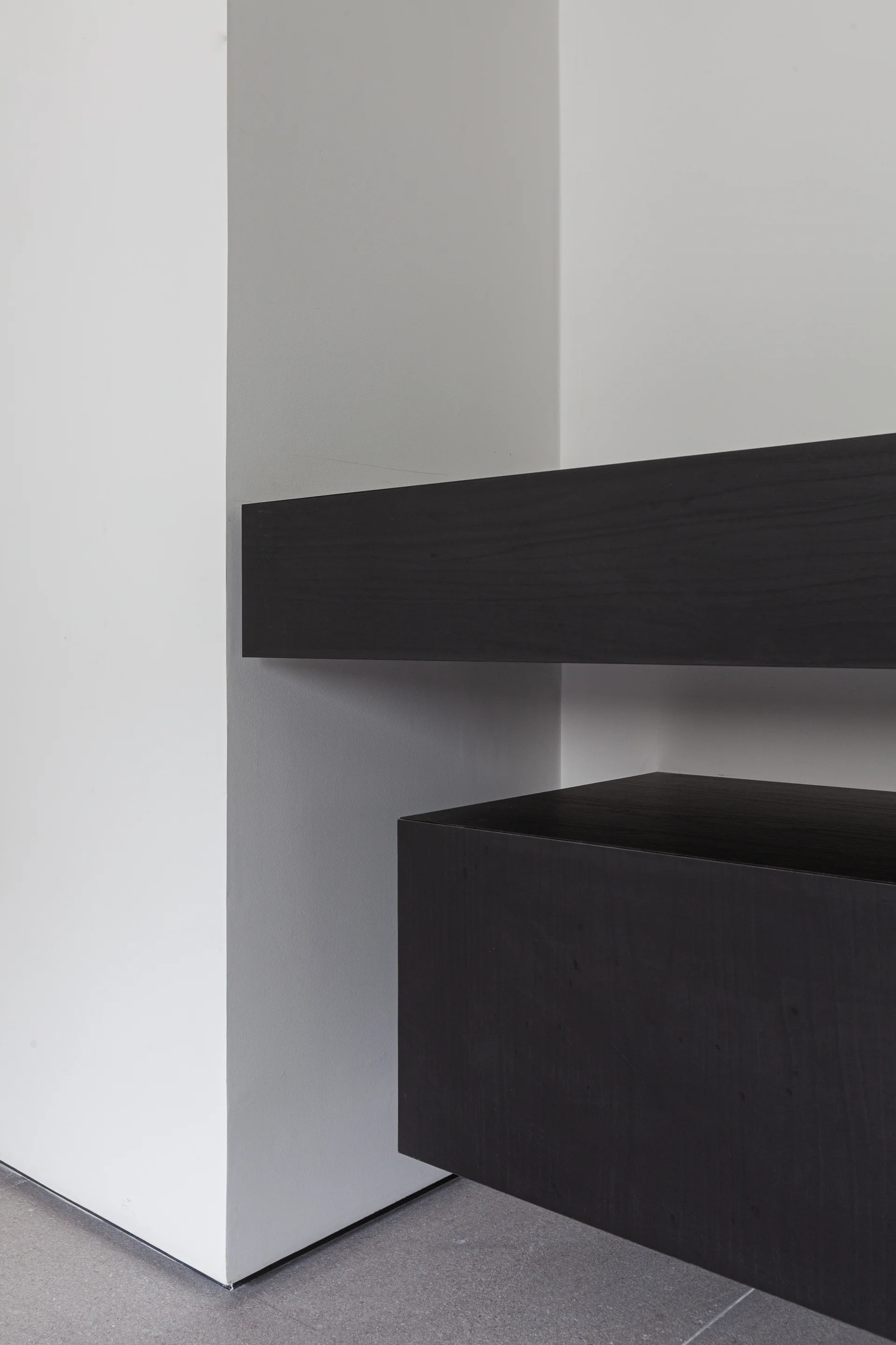 A close-up of dark wood floating shelves and a block cabinet mounted against a white corner wall with grey flooring.
