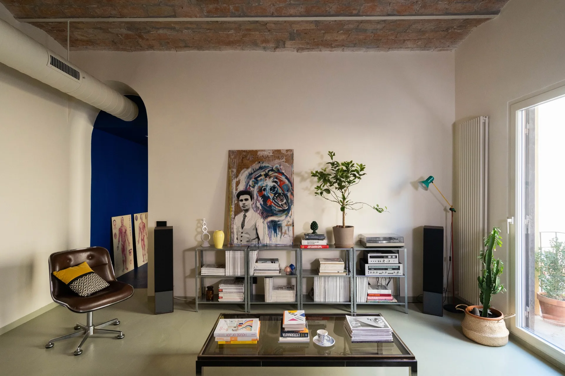 An eclectic living room features a vaulted brick ceiling, a blue arched entryway, low metal shelving, and a brown leather swivel chair.