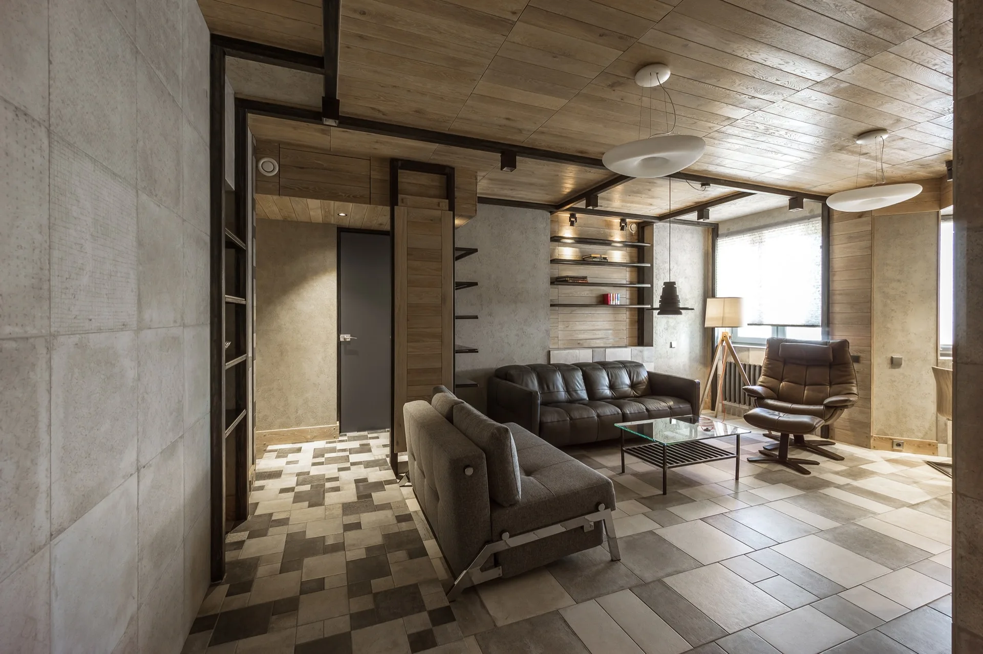 A contemporary living room featuring a gray sofa, a brown leather recliner, a wood-plank ceiling, and patterned geometric floor tiles.