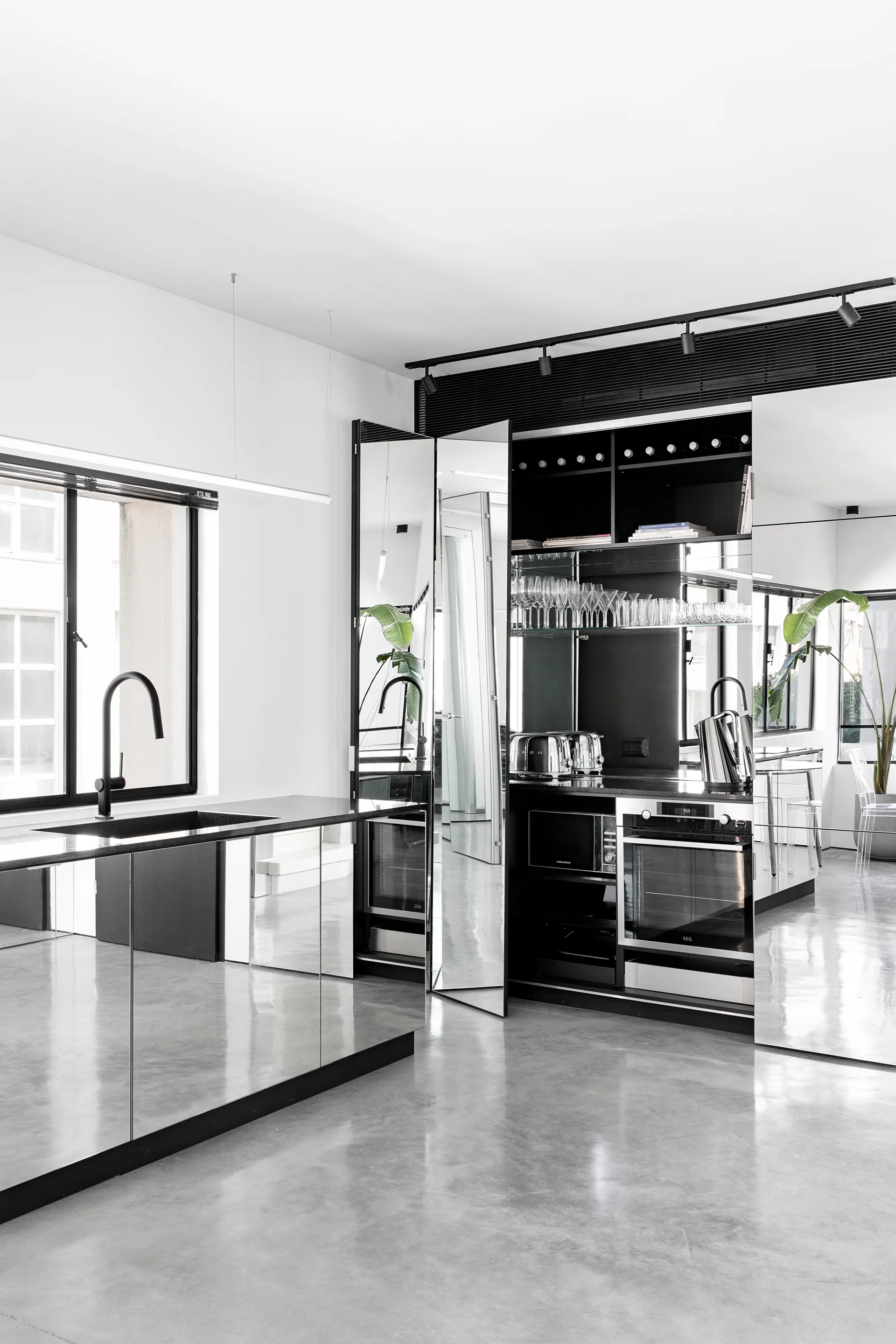 A minimalist modern kitchen featuring a mirrored island, matte black faucet, and built-in black cabinetry with reflective panels on polished concrete.