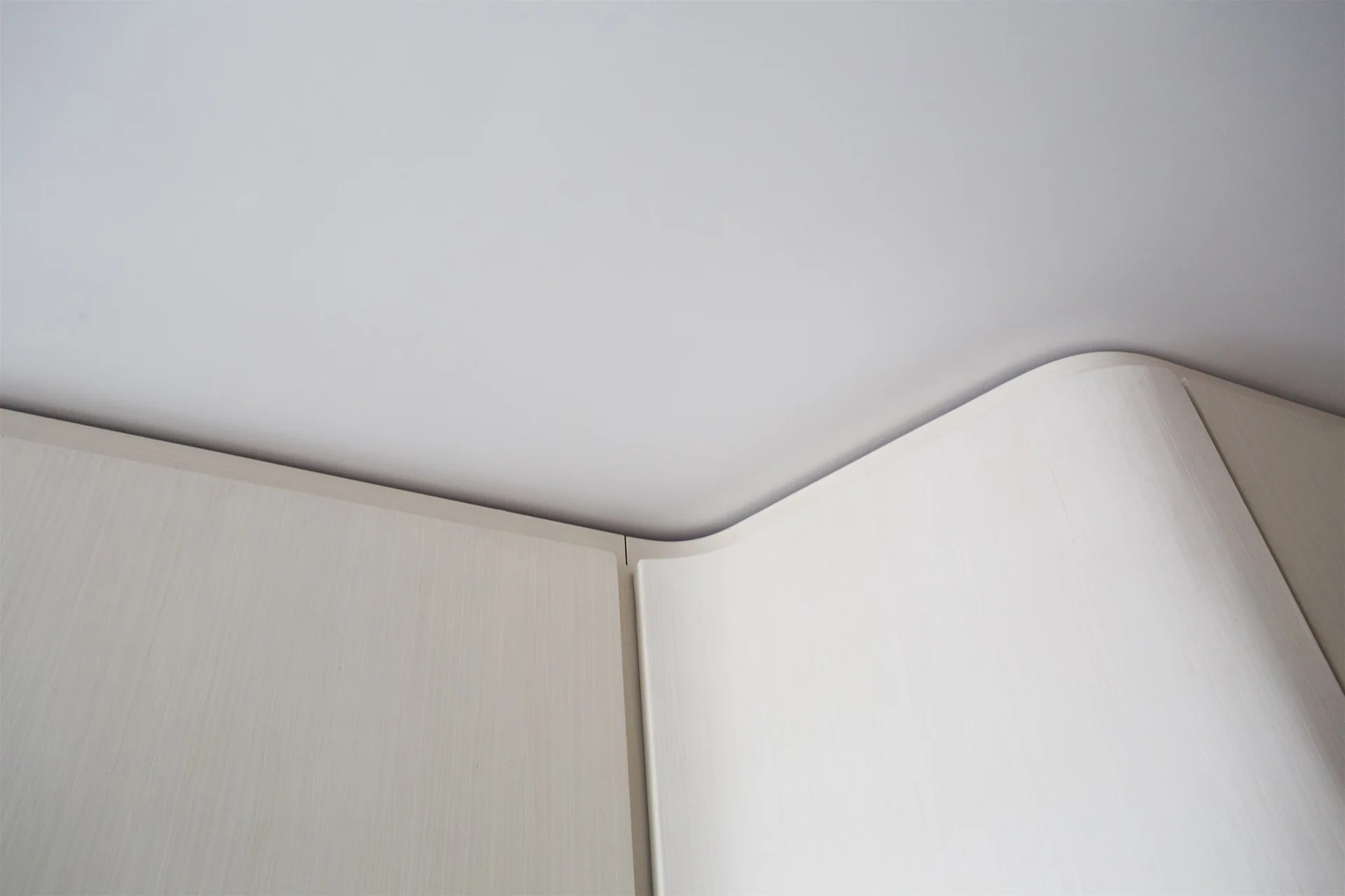 A close-up view of light cream cabinetry with a rounded, curved corner meeting a flat white ceiling.