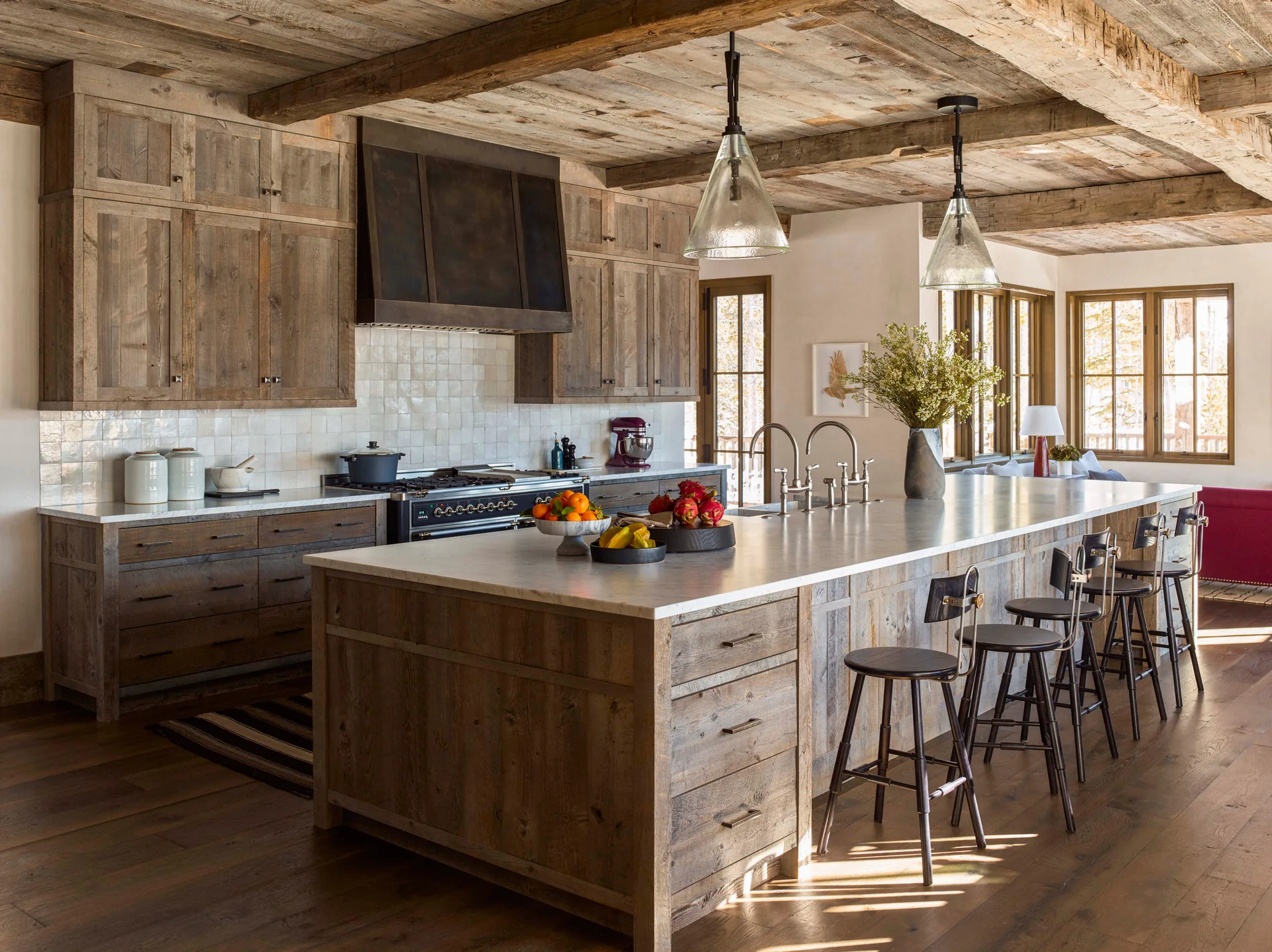 A rustic kitchen featuring reclaimed wood cabinetry, a large marble-topped island with black bar stools, and two glass pendant lights.