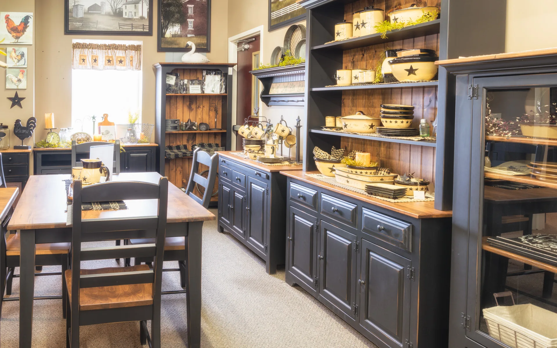 A rustic room displays black painted wooden hutches, a matching dining table, and cream ceramic dinnerware on open shelves.
