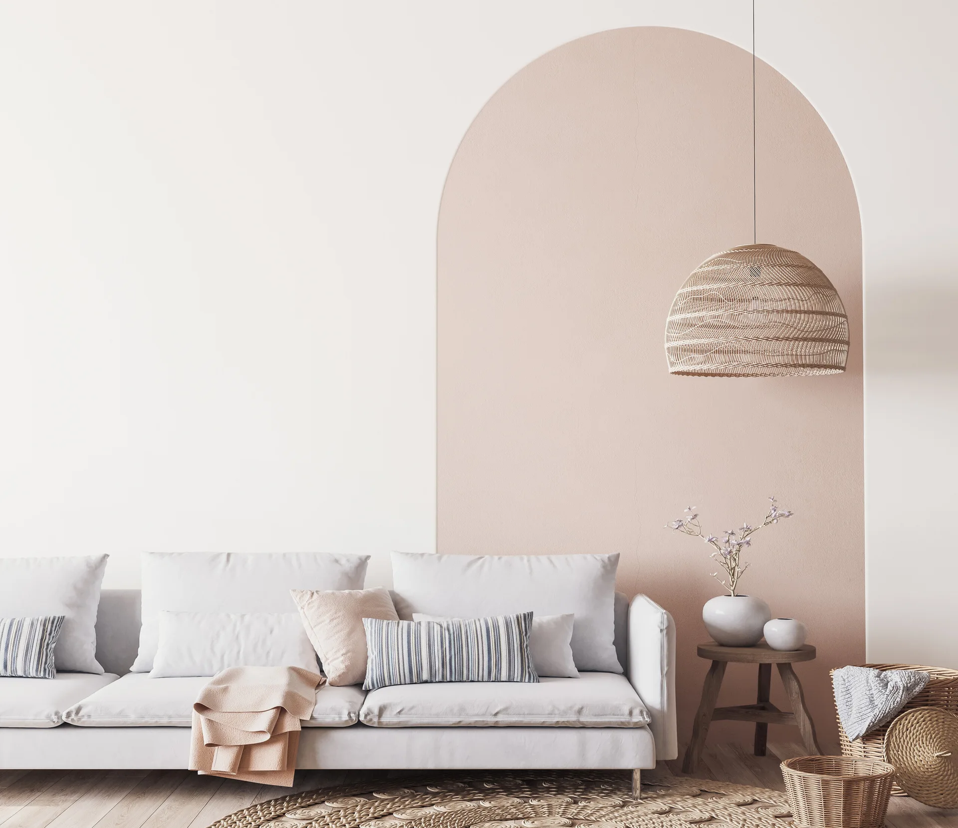 A light-toned living room features a white sofa with striped pillows against a wall painted with a blush pink decorative arch.