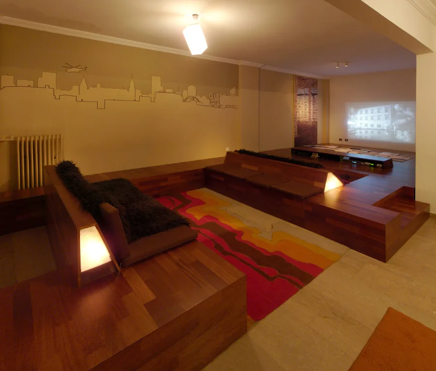 A media room features custom multi-level wood platform seating, a wavy pattern area rug, and a skyline mural on the wall.