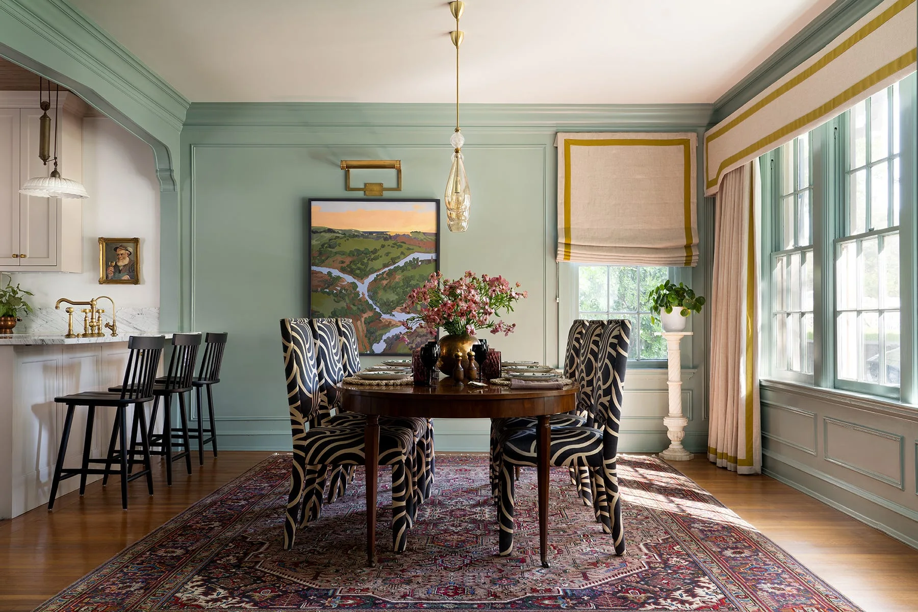 A traditional dining room with sage green paneled walls, a dark wood table surrounded by zebra-print chairs, and a large patterned rug.