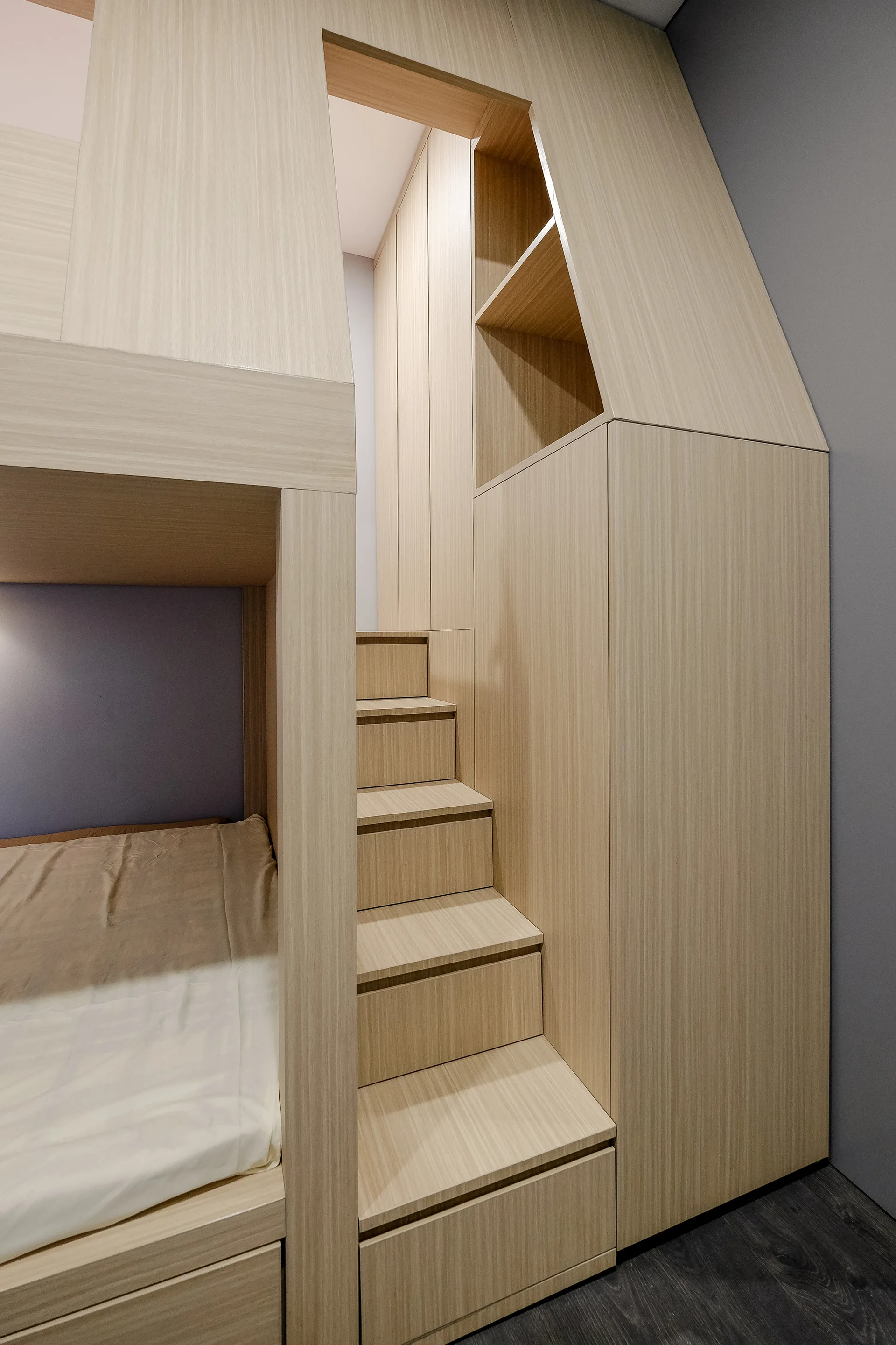 A custom light wood bunk bed features integrated staircase steps and a recessed display niche against a grey bedroom wall.