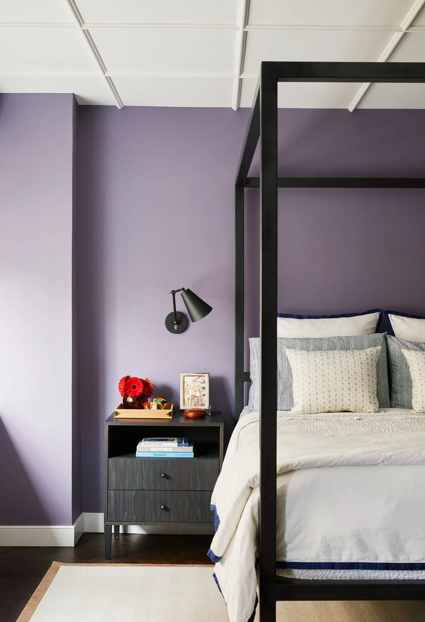 A bedroom featuring a black metal canopy bed, lavender painted walls, a dark wood nightstand, and a white paneled ceiling.