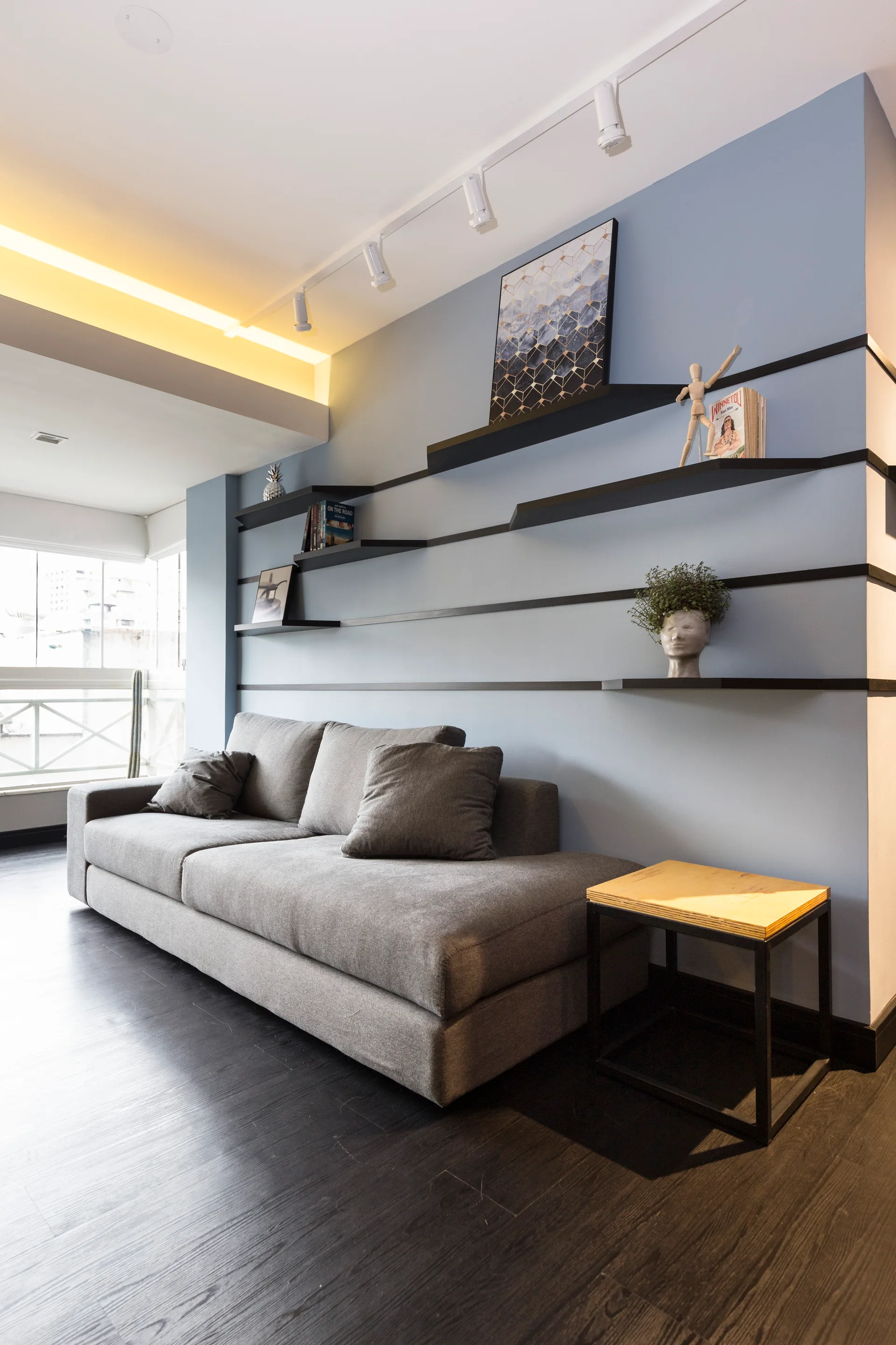 A grey fabric sofa sits against a light blue wall detailed with continuous black horizontal lines that form staggered display shelves.