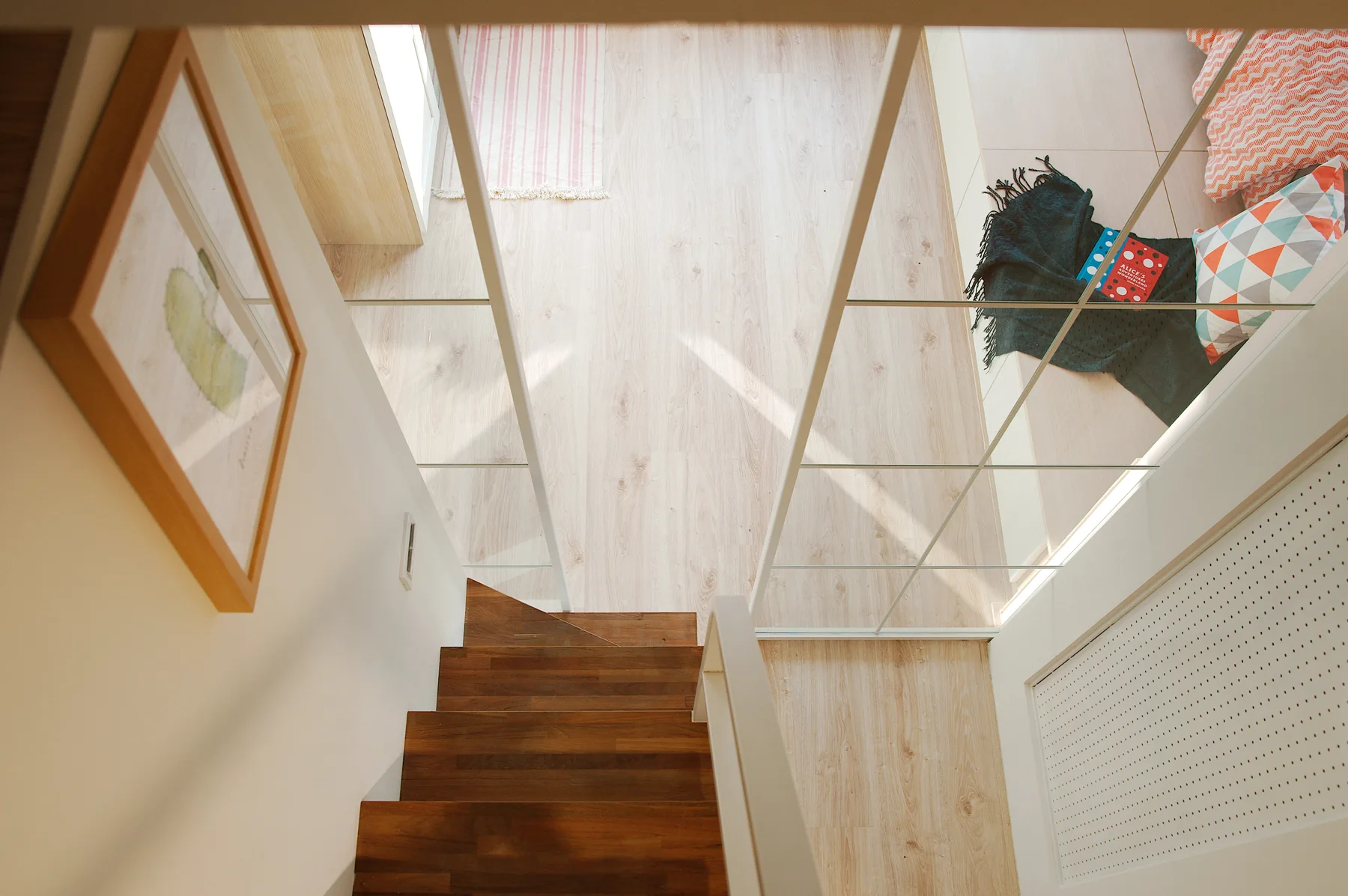 An overhead view looking down a dark wood staircase onto light wood floors, a white metal grid railing, and a platform bed.