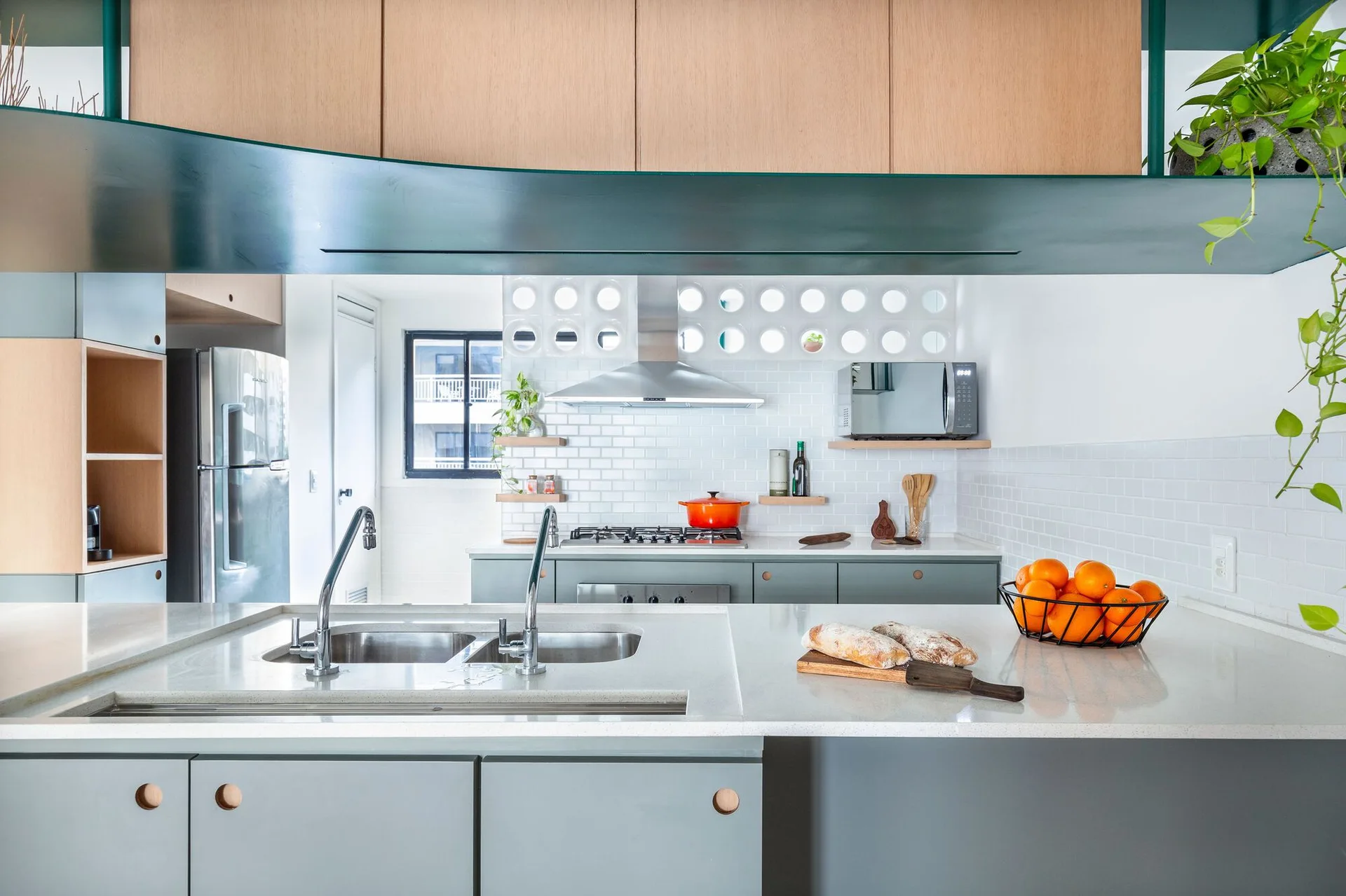 A modern kitchen features a grey island with a double sink, wood upper cabinets, and a decorative white breeze block screen behind the stove.