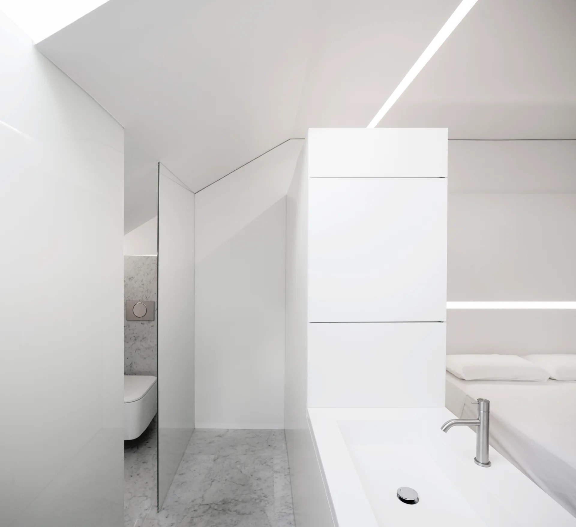 A minimalist white bedroom featuring an integrated sink with a chrome faucet next to a glass partition and marble flooring.