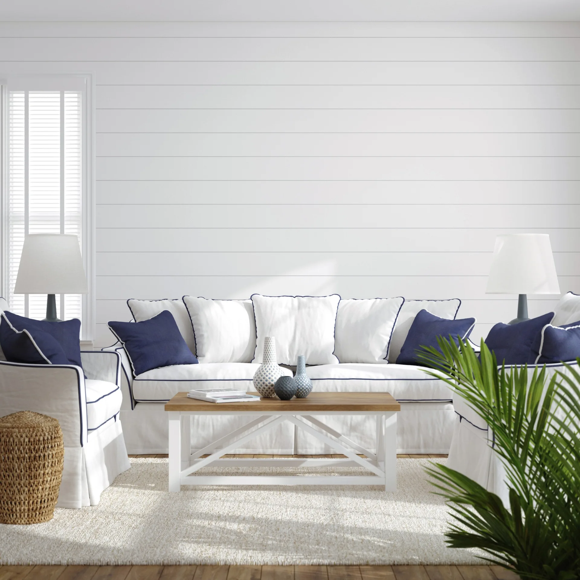 A coastal living room features a white sofa with navy piping, a wood-topped coffee table, and a white shiplap accent wall.