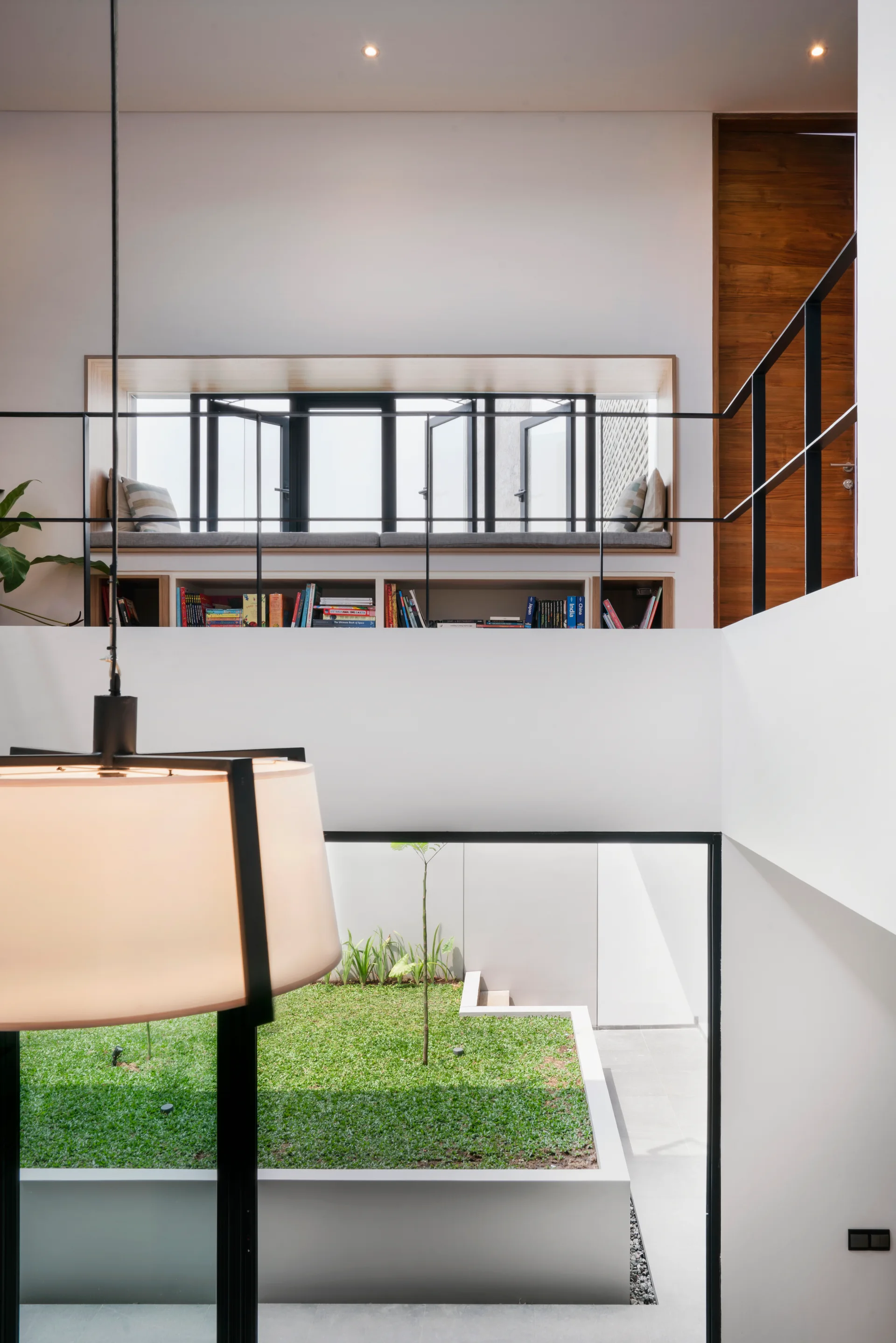 A modern multi-level landing featuring a built-in window seat with under-seat bookshelves overlooking a central lightwell courtyard with grass below.