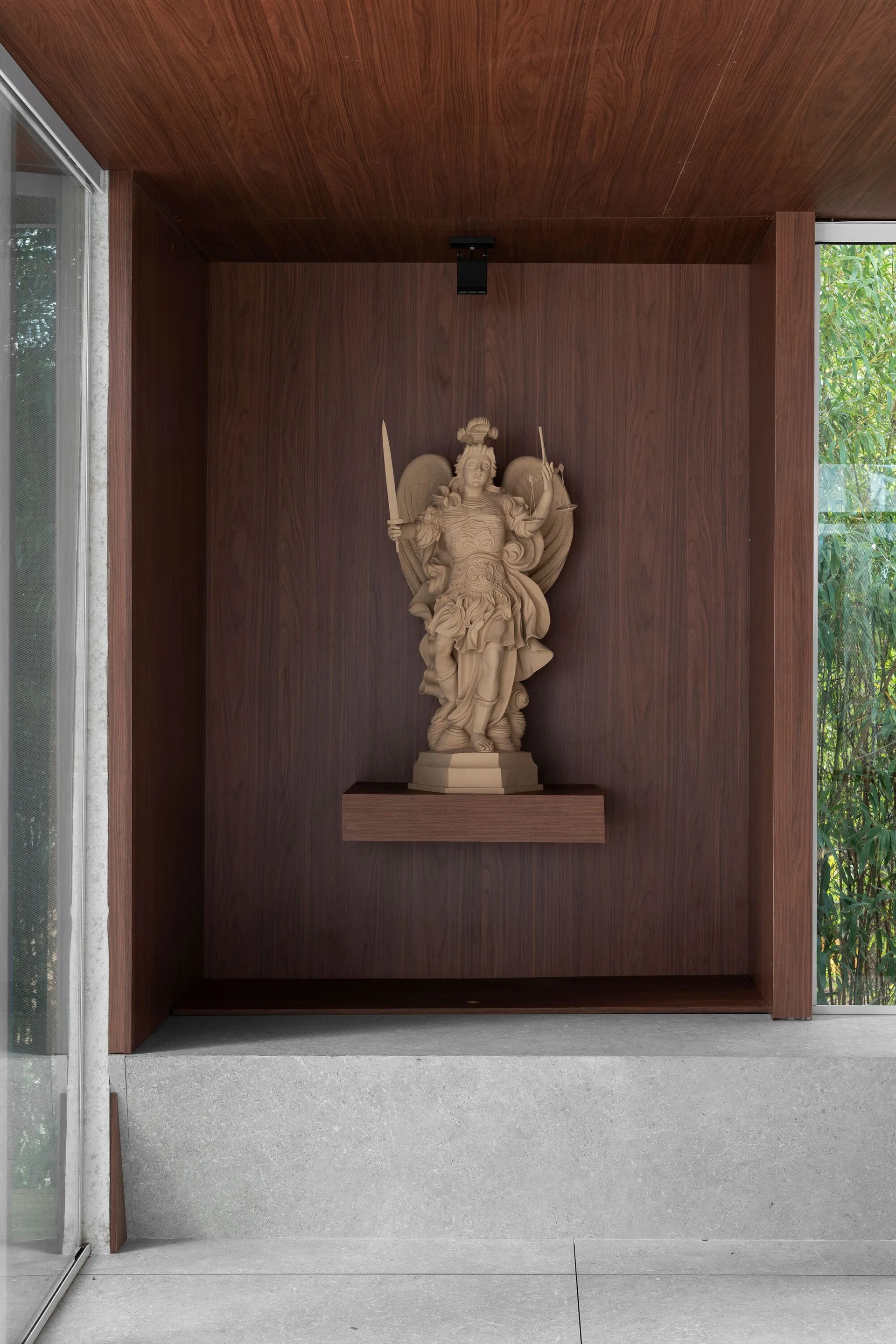 A beige classical warrior statue stands on a floating wooden shelf inside a dark wood-paneled wall niche above a gray stone ledge.