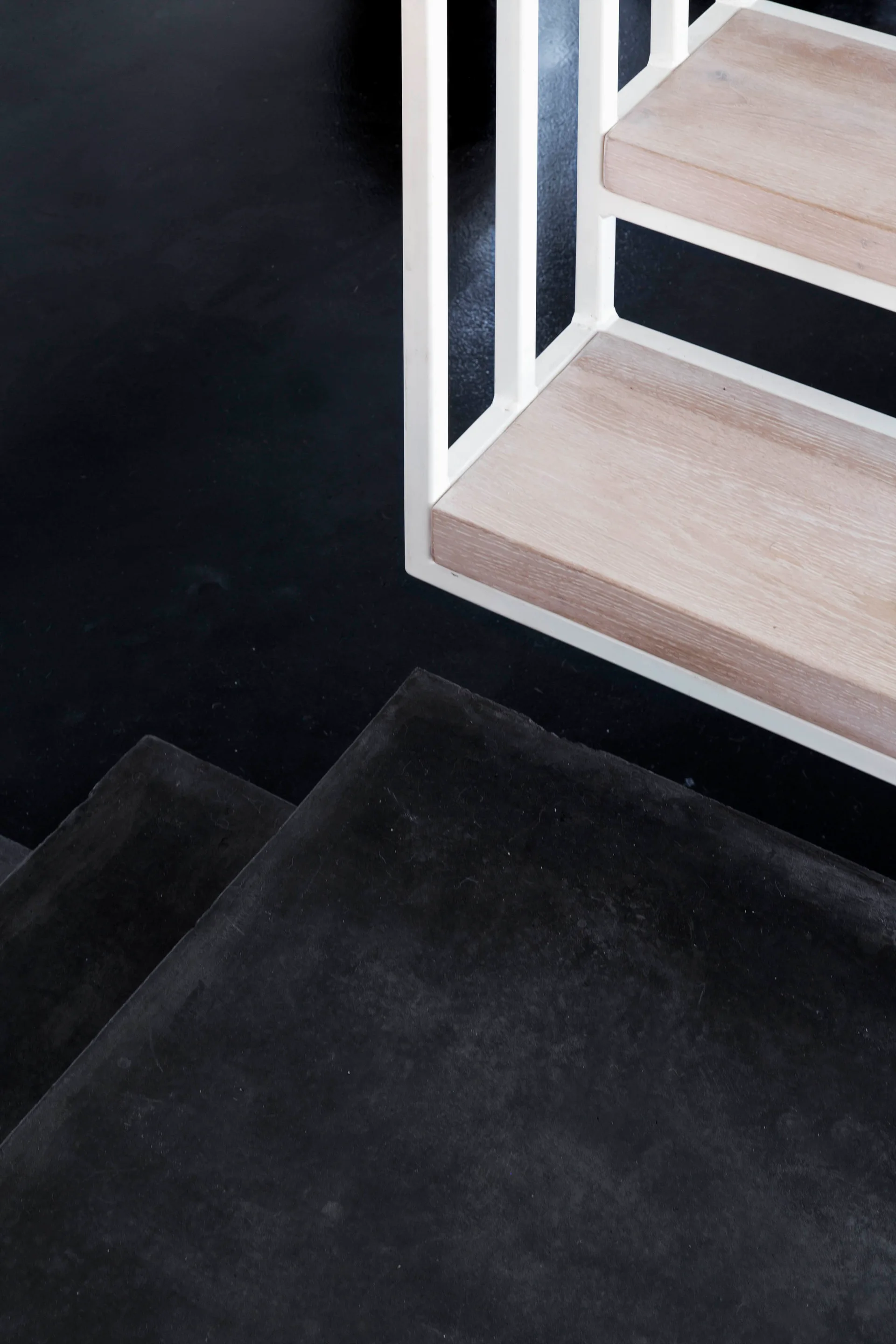 A minimalist staircase detail featuring light wood treads with a white metal railing next to matte black steps.