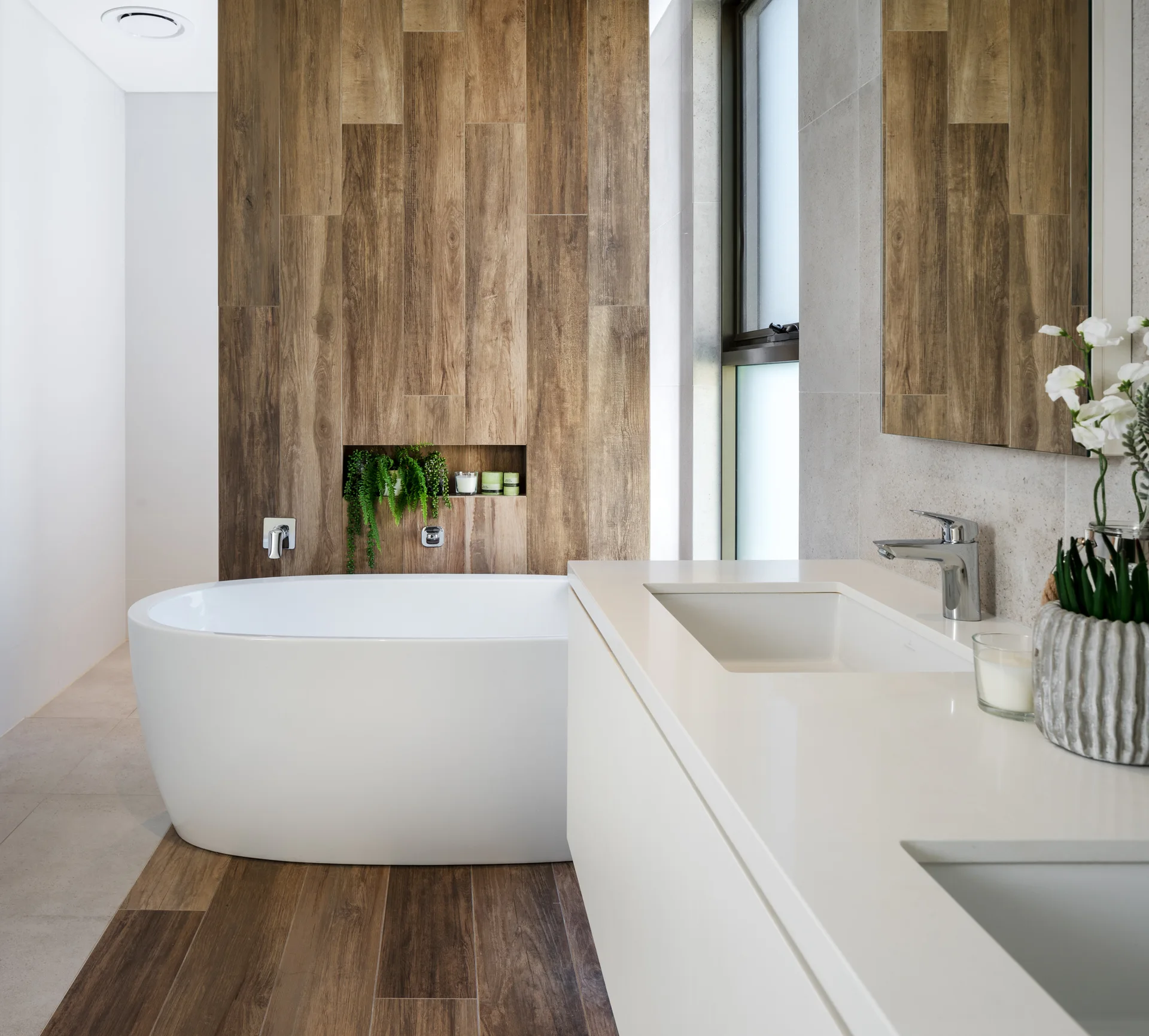 A modern bathroom featuring a white freestanding bathtub positioned against a wood-plank accent wall next to a sleek white vanity with a chrome faucet.