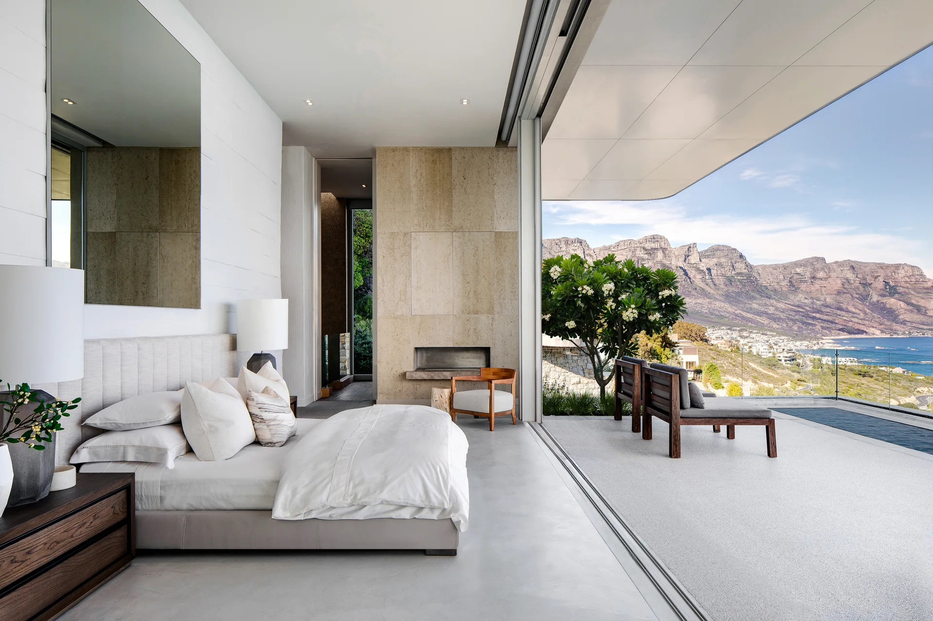A minimalist bedroom with a platform bed opens through a large sliding glass door to a concrete patio with a scenic mountain view.