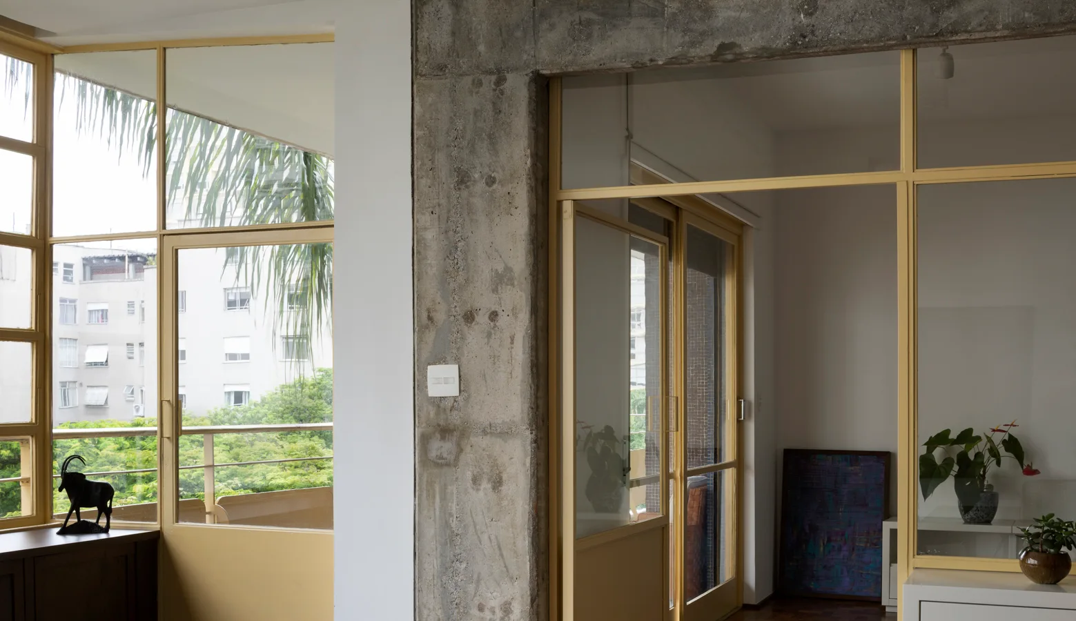 An apartment interior features an exposed concrete column alongside yellow-framed glass partition walls and windows.