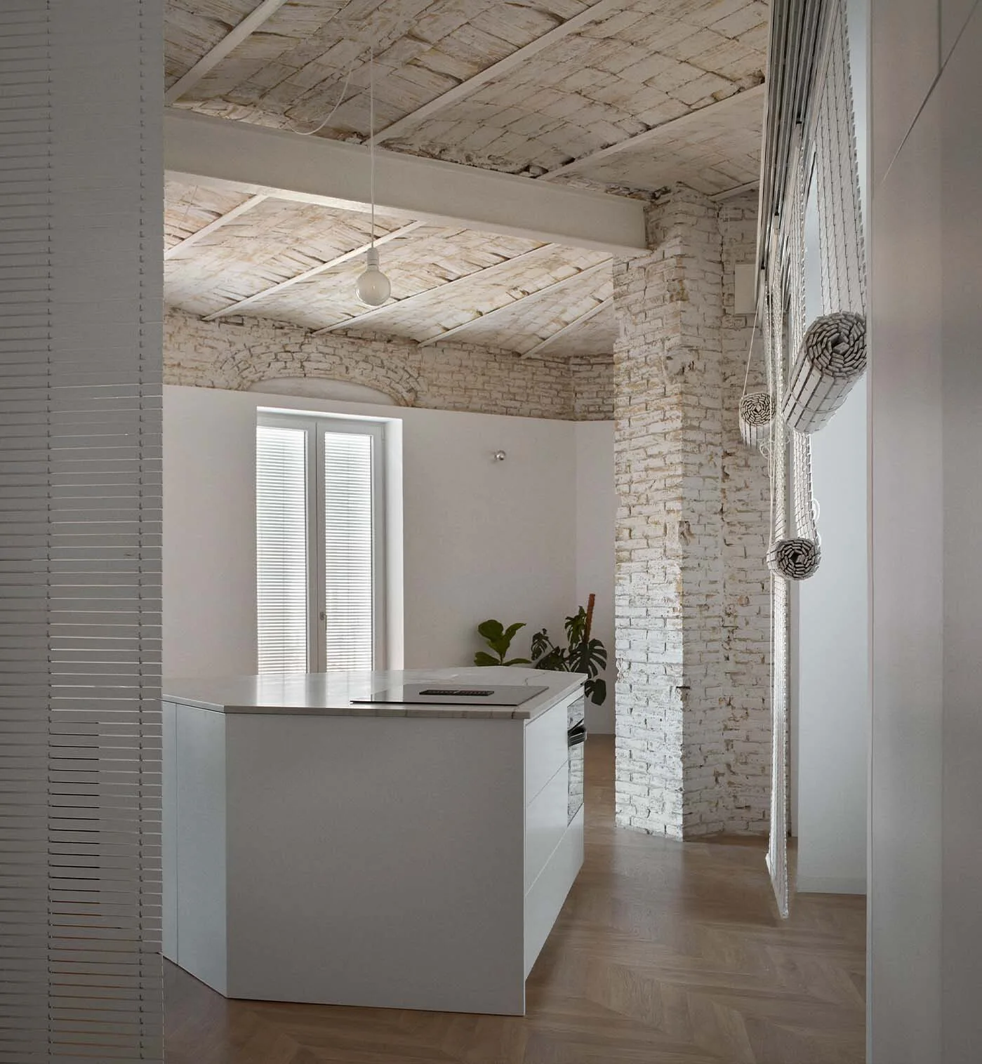 A white kitchen island sits on herringbone wood flooring beneath a vaulted, white-washed brick ceiling with a single pendant bulb.