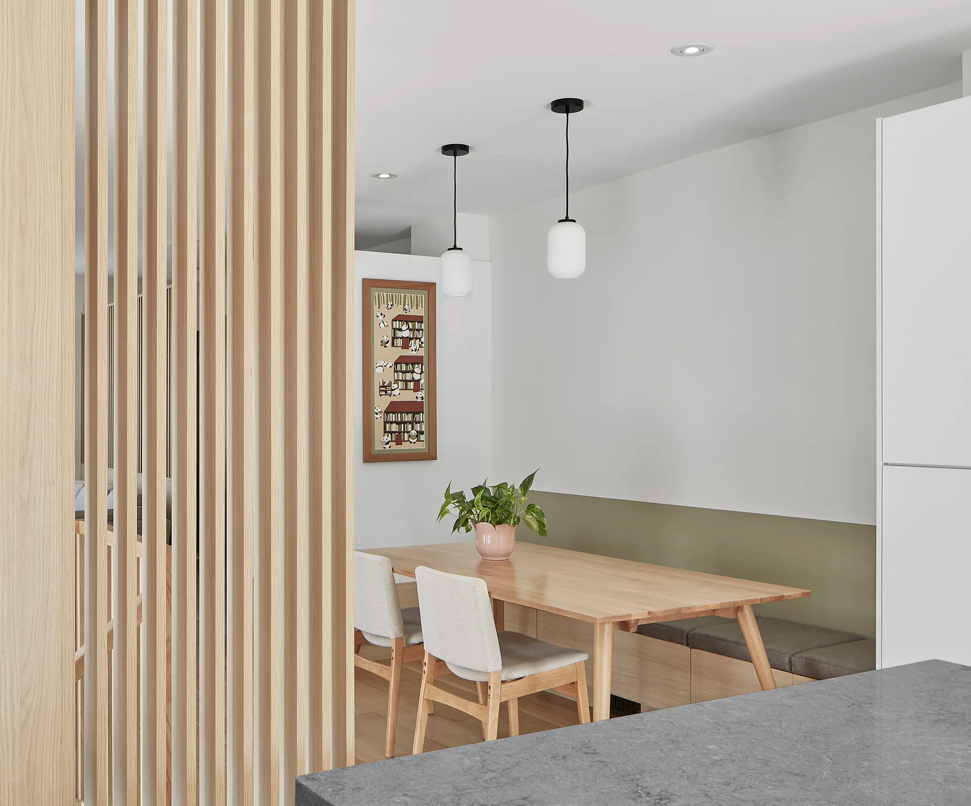 A light wood dining table with upholstered chairs and a built-in bench next to a tall vertical wood slat partition wall.