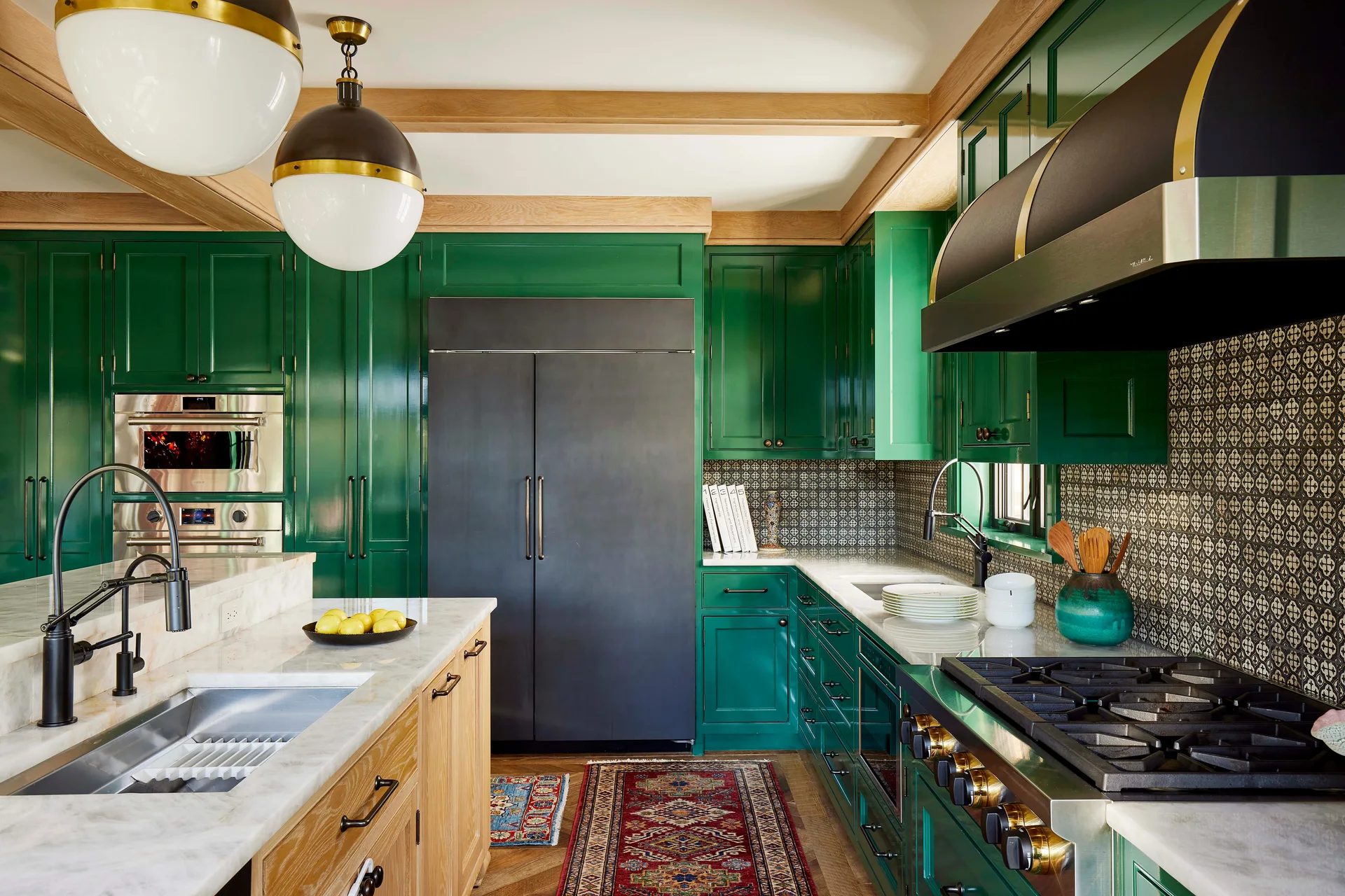 A modern kitchen with high-gloss emerald green cabinets, a marble countertop island, a patterned black and white backsplash, and wood ceiling beams.