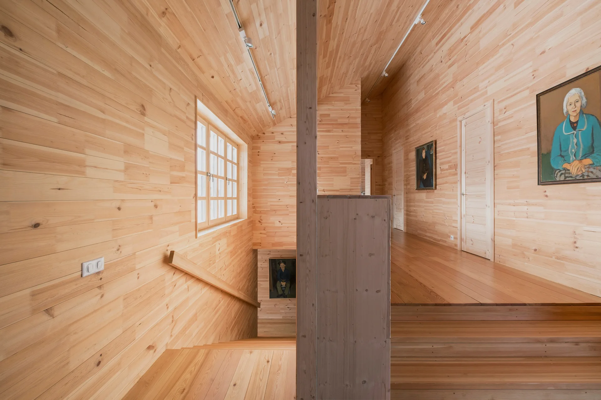 A staircase and hallway featuring light wood plank walls, matching ceilings, a grid-style window, and several framed portraits on the walls.