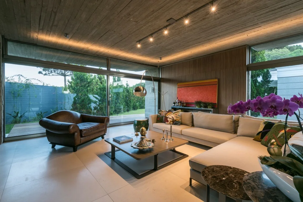 A contemporary living room featuring a concrete ceiling, large sliding glass doors, a cream sectional sofa, and a brown leather armchair.