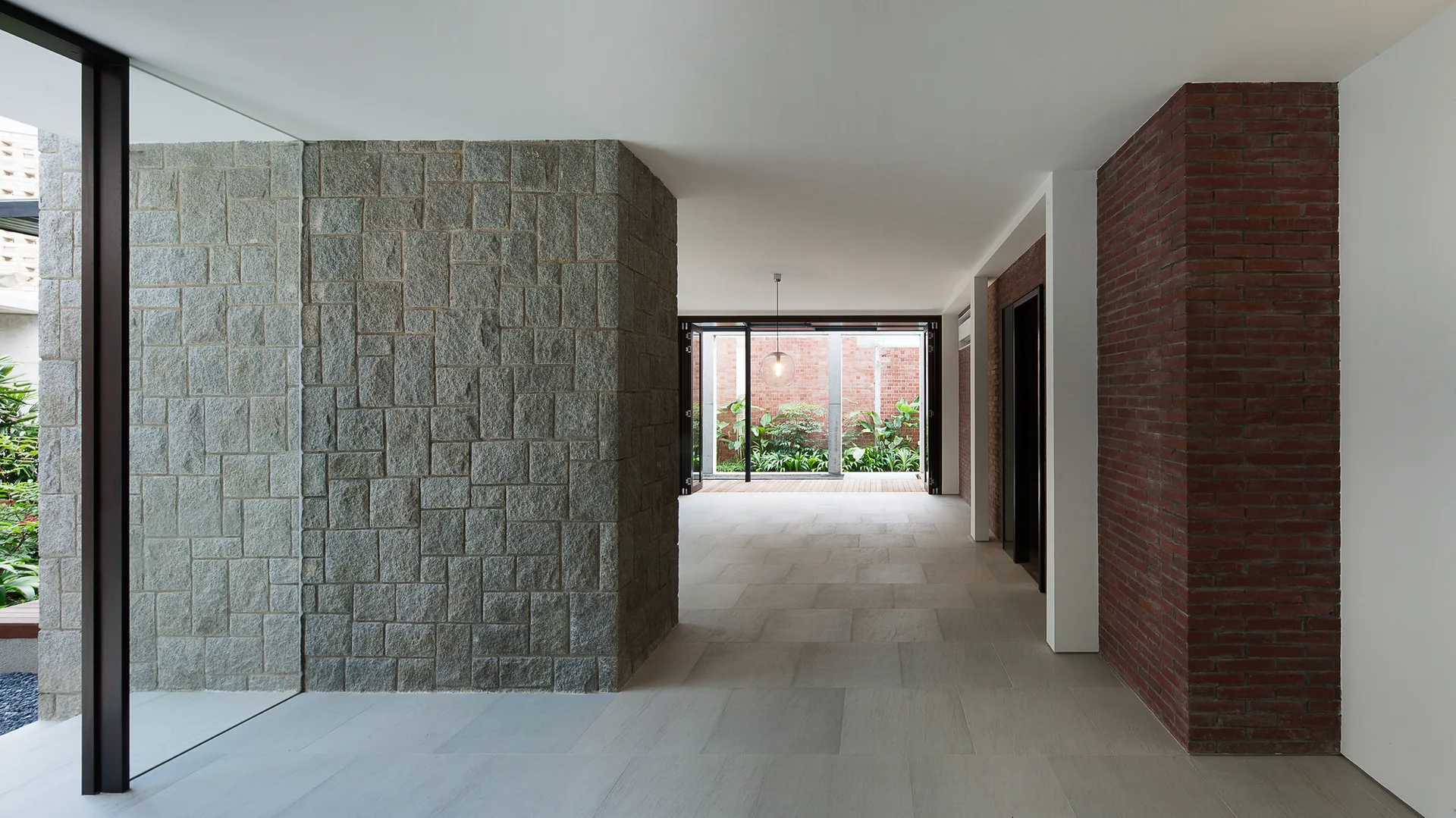 A minimalist hallway features a grey stone block wall on one side and a red brick wall on the other, leading to a courtyard garden.