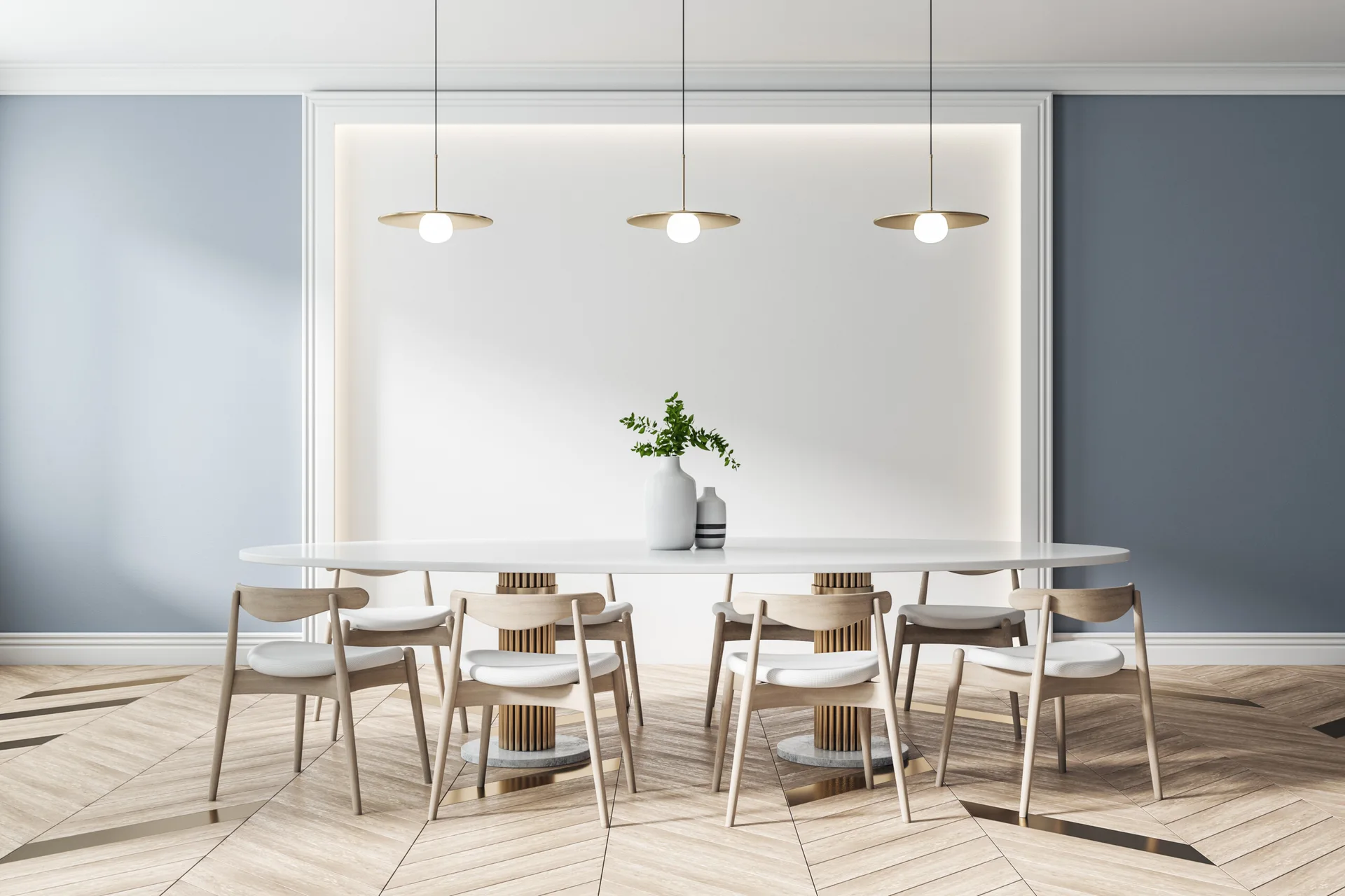 A modern dining room featuring a white oval table, wooden chairs, and three gold pendant lights against a blue wall with a glowing recessed panel.