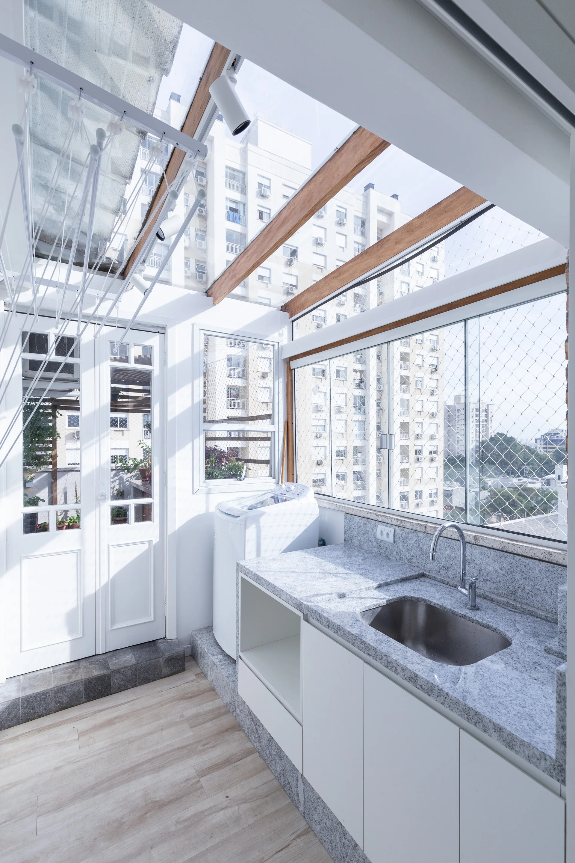 A bright utility room features a speckled stone countertop with a sink, a washing machine, and a glass roof with exposed wood beams.