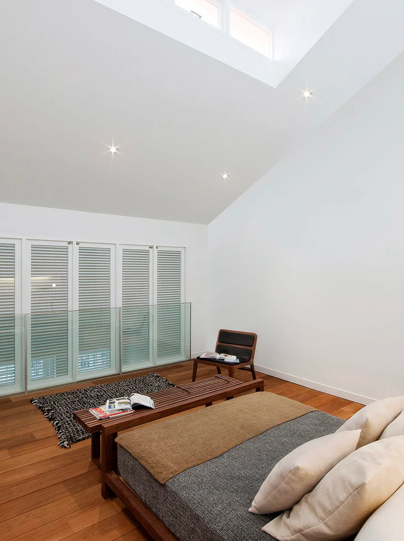 A loft bedroom featuring a low-profile bed, a slatted wooden bench, warm hardwood floors, and a sloped ceiling with a skylight.