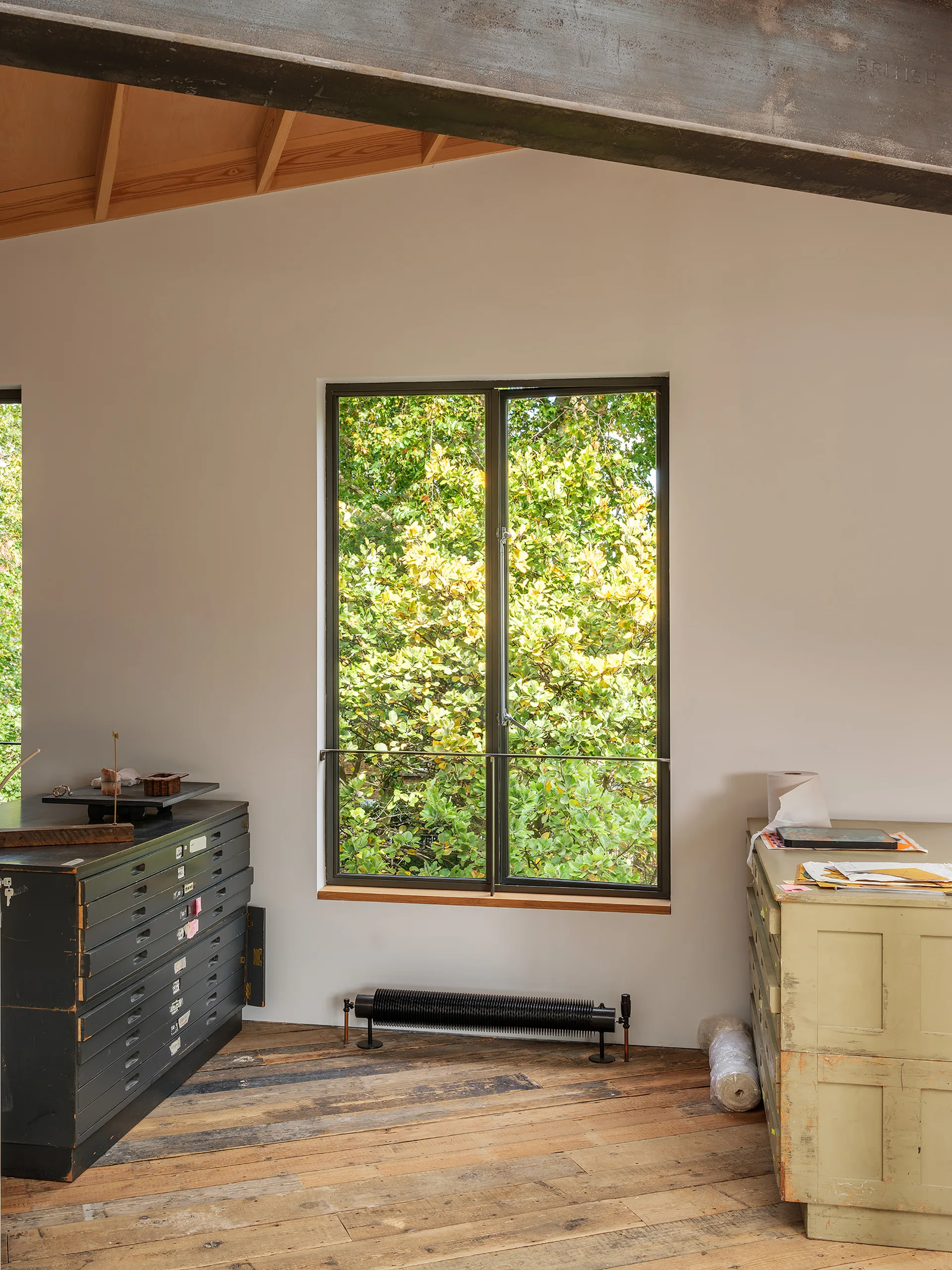 A workspace with weathered wood floors and a large rectangular window showing leafy green trees between two vintage storage cabinets.