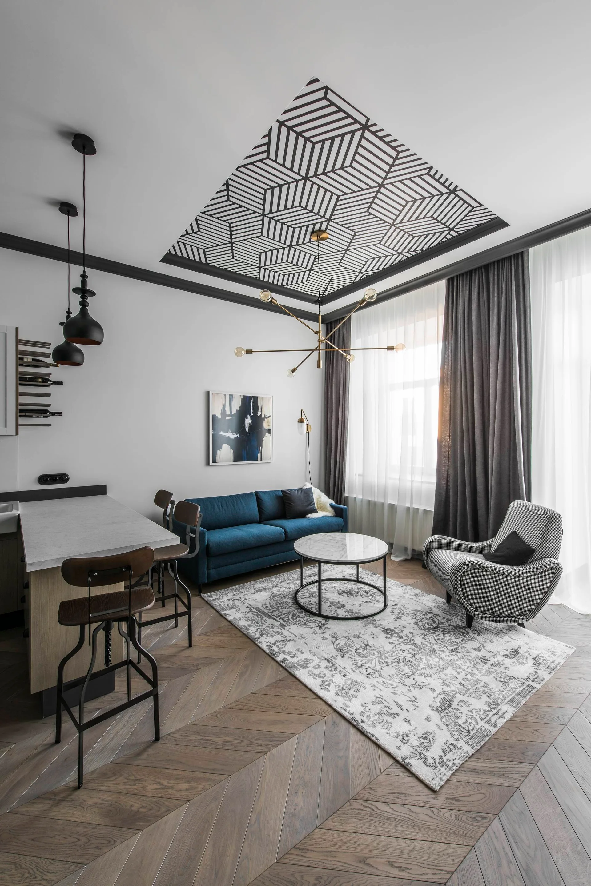 A contemporary living room features a blue sofa, a houndstooth armchair, herringbone wood floors, and a bold geometric pattern on the ceiling.