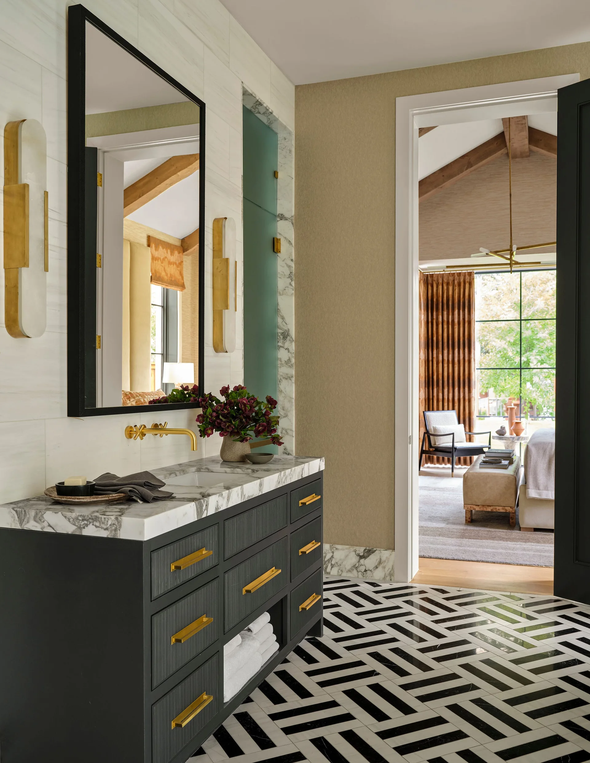 A modern bathroom features a dark fluted vanity with a veined marble countertop, gold fixtures, and a black and white herringbone tile floor.