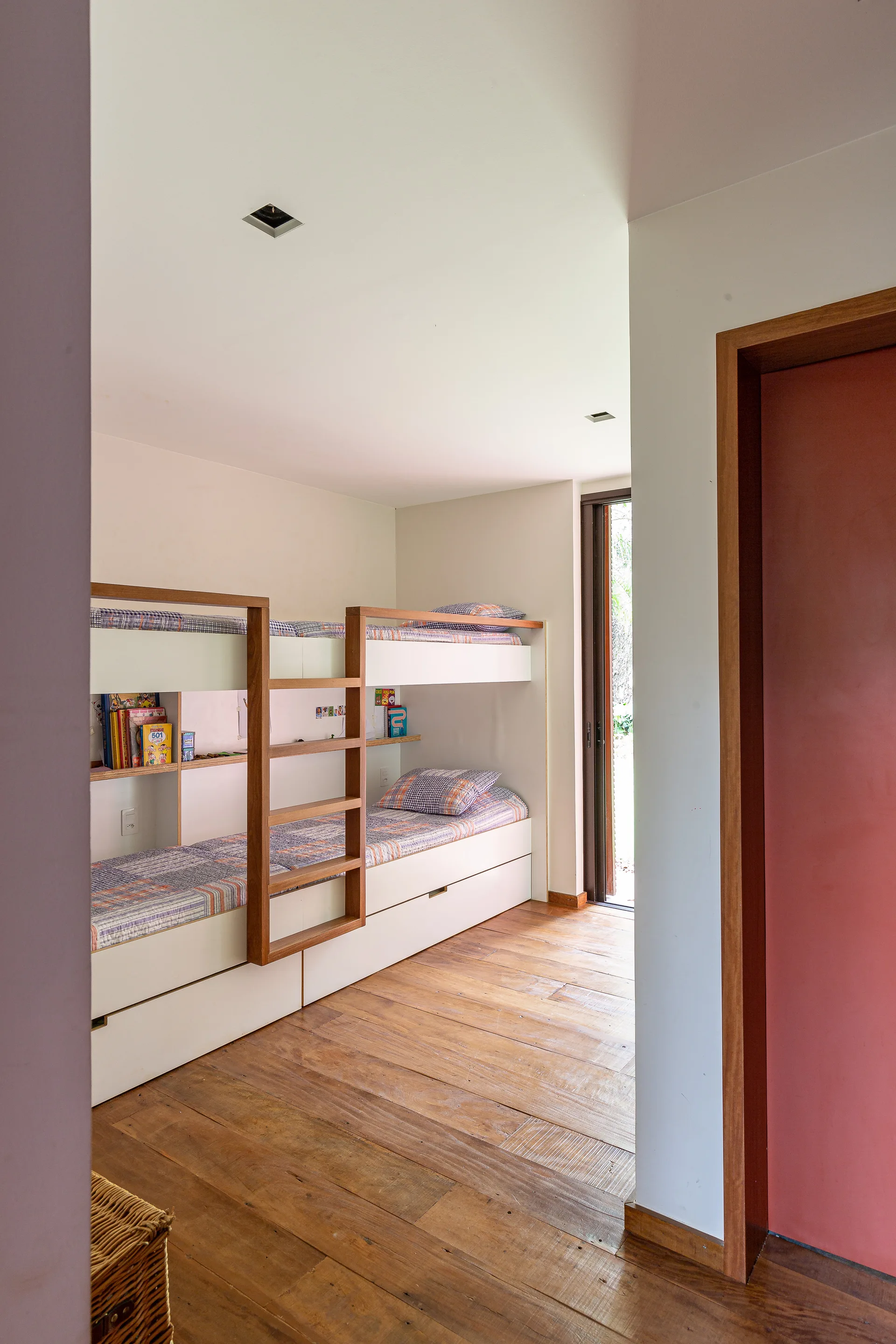 A minimalist kids bedroom features a white and natural wood built-in bunk bed set on wide hardwood plank floors.