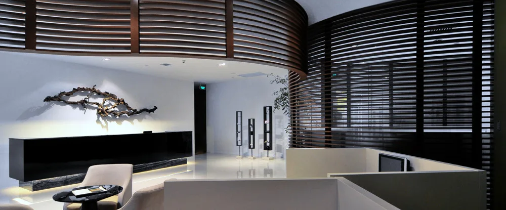 A modern lobby reception area features a glossy black desk, white tiled floors, and a curved wooden slat partition screen.