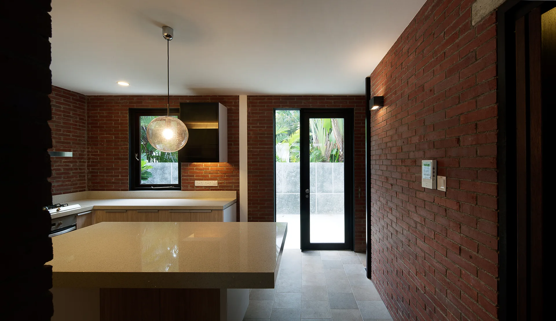 A contemporary kitchen featuring exposed red brick walls, a large stone-like island, and a glass door leading outside.