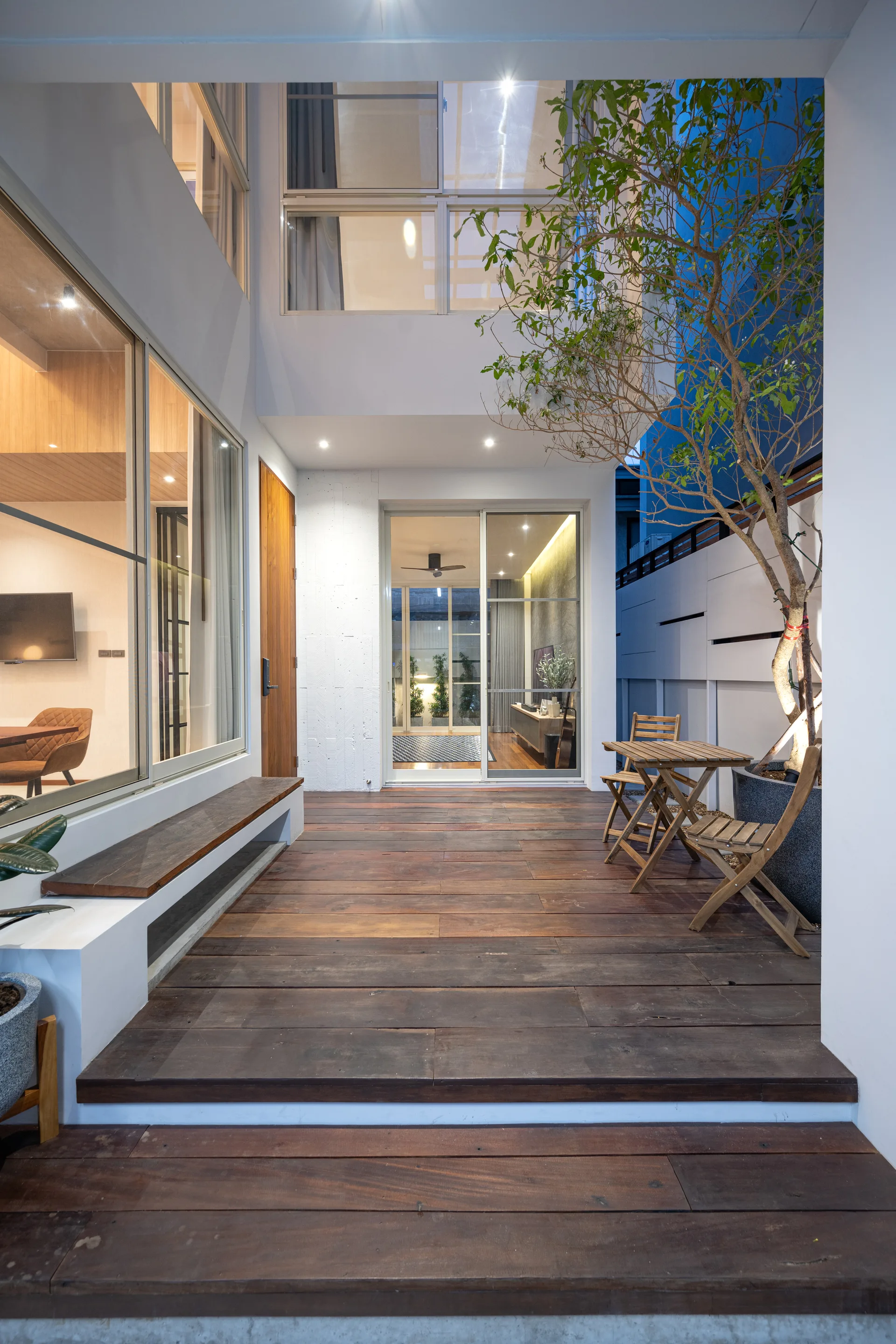 A multi-level wooden deck patio features a built-in white bench with a wood seat, a small folding bistro table with chairs, and a sliding glass door.