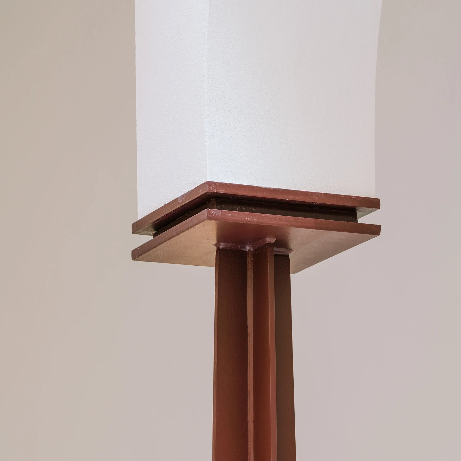 Close-up of a brown structural metal column meeting a painted white archway with a square metal plate junction.