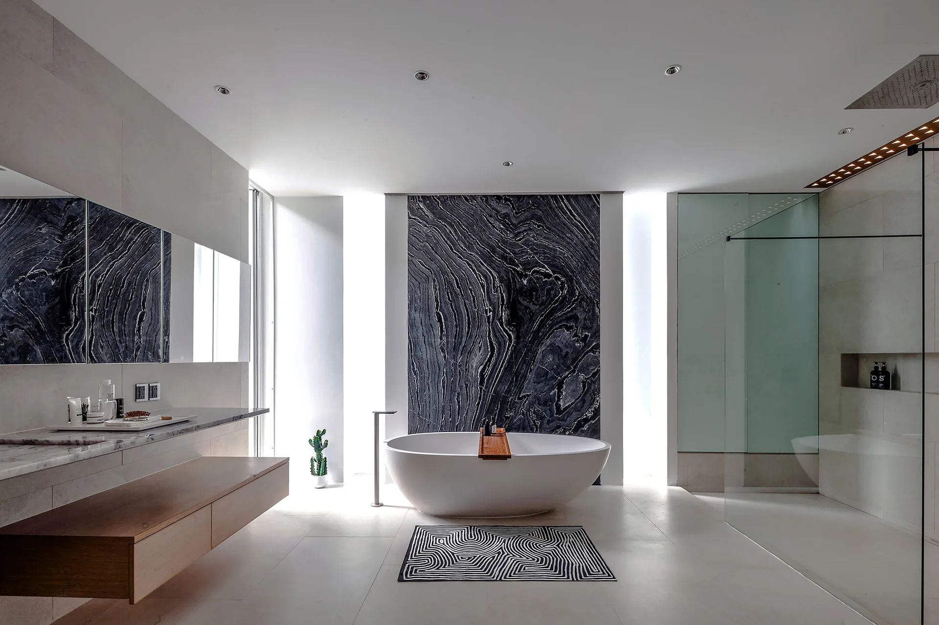 A modern minimalist bathroom featuring a white freestanding bathtub positioned in front of a large black veined marble accent wall.