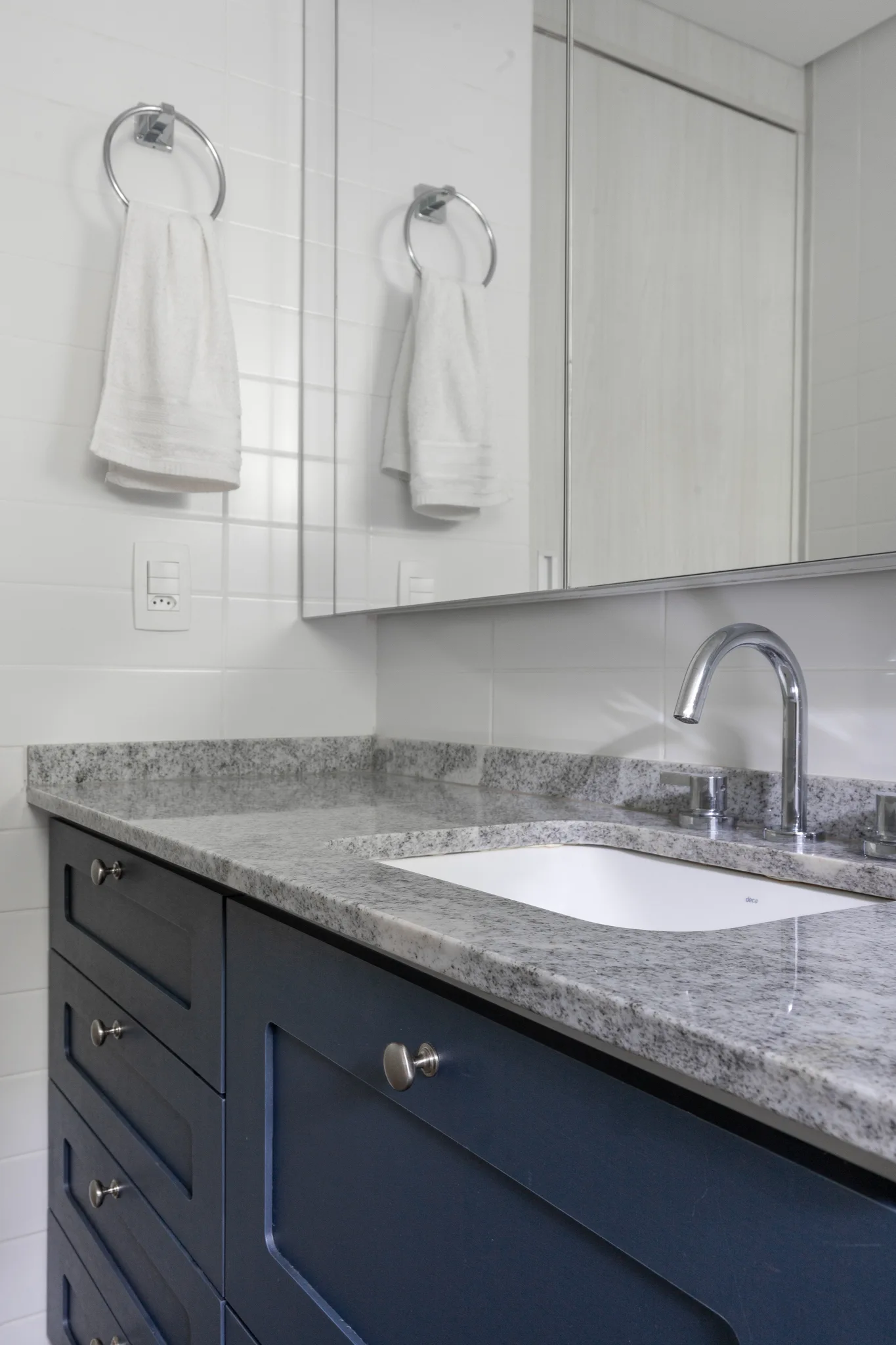 A bathroom vanity features deep blue cabinets with shaker doors, a speckled grey stone countertop, an undermount sink, and a white tiled wall.