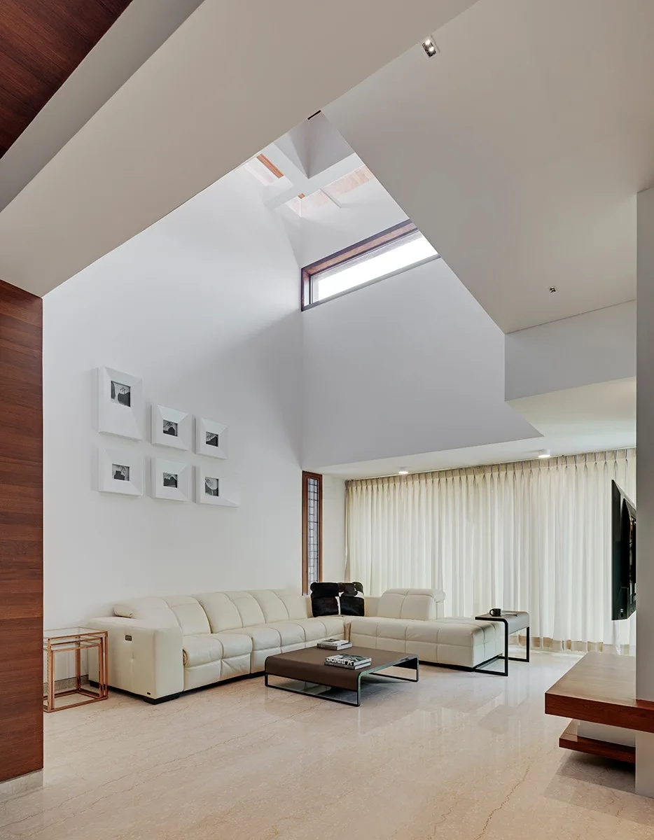 A double-height living room features a cream leather sectional sofa, a low brown coffee table, and a grid gallery wall under a skylight.