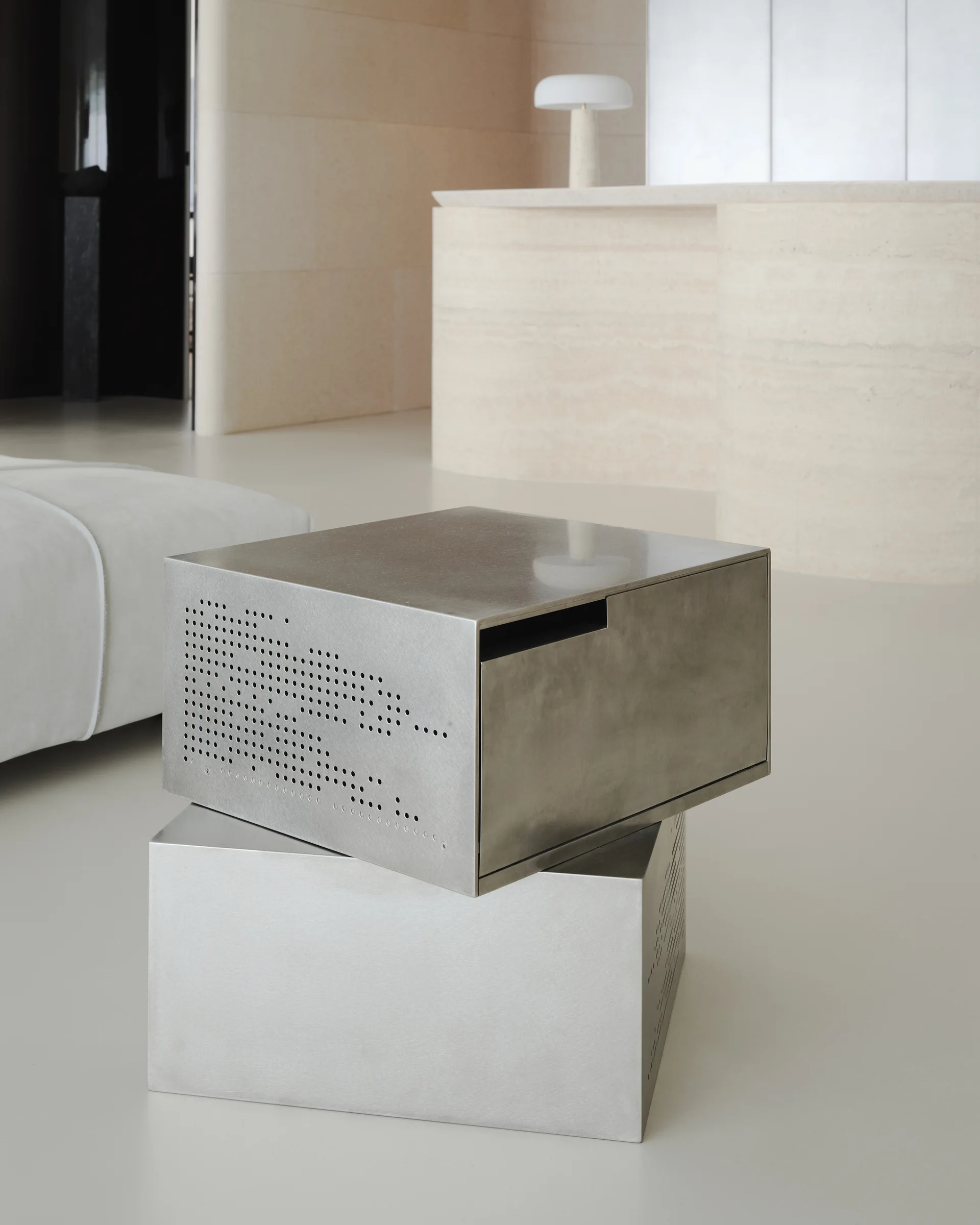 Two modular brushed metal box tables are stacked offset on a smooth floor near a curved beige stone counter.