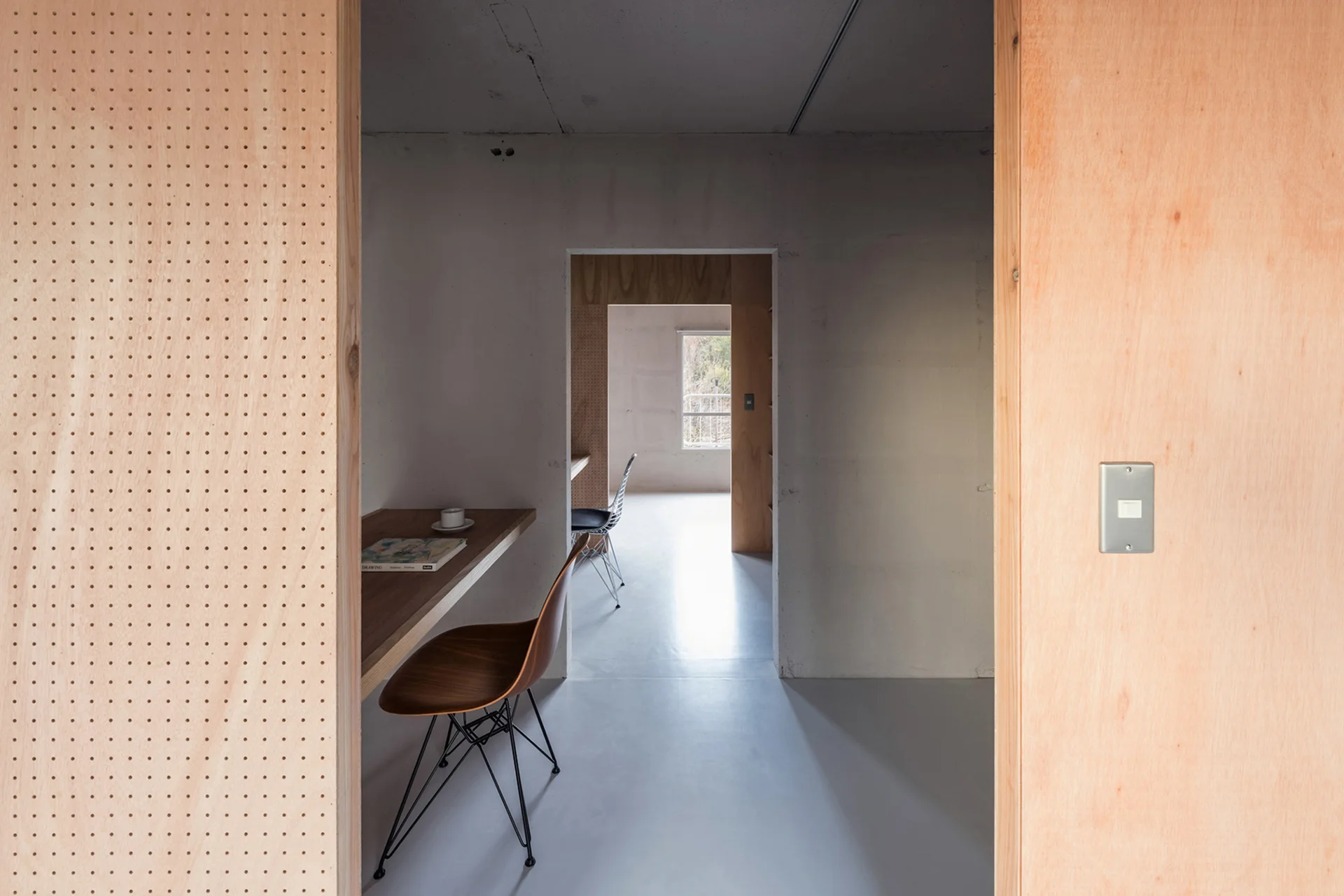 View through a doorway into a minimalist home office featuring plywood paneling, a floating wooden desk, and a mid-century desk chair.